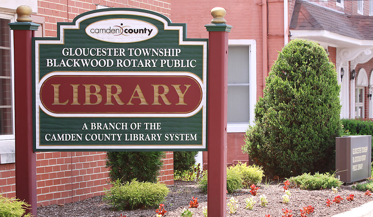 Sign with red posts on either side with a green background and white lettering of the library name and the word library in gold large in the middle set against red.
