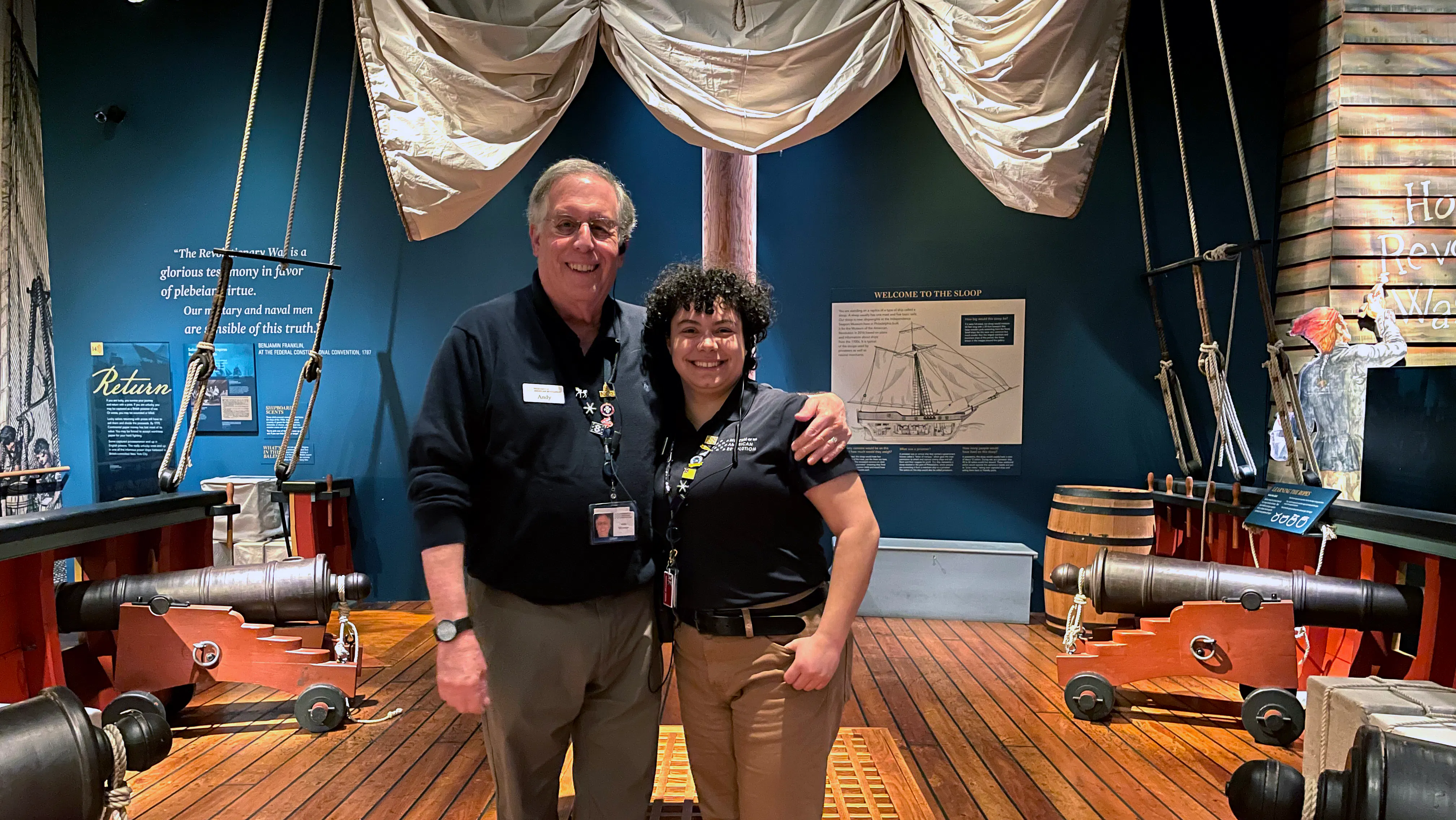 Two people in uniform stand on the replica ship in the Museum's galleries