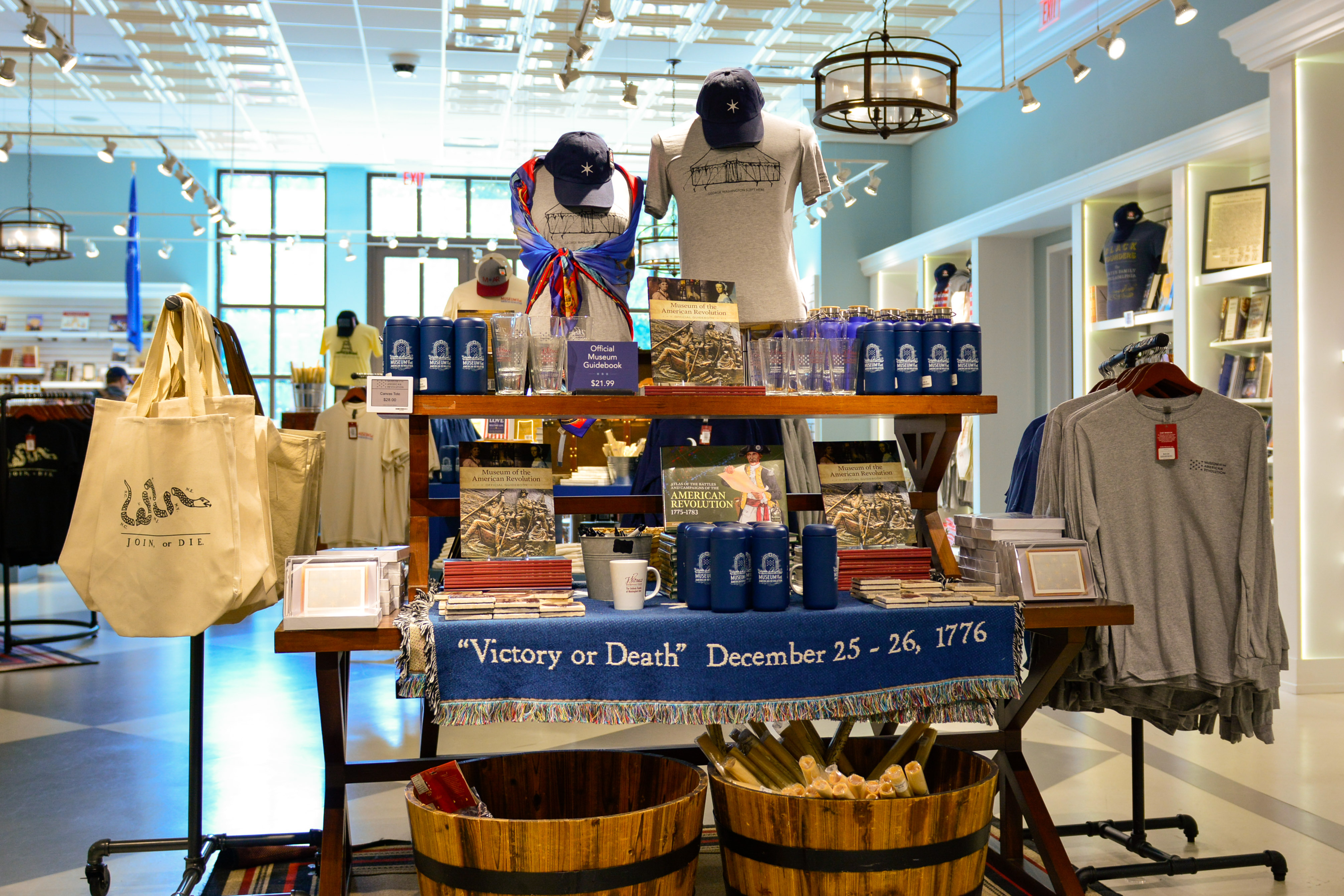 This image shows a display of Museum merchandise including tote bags, mugs, tee shirts, scarves, and more in the Museum Shop.