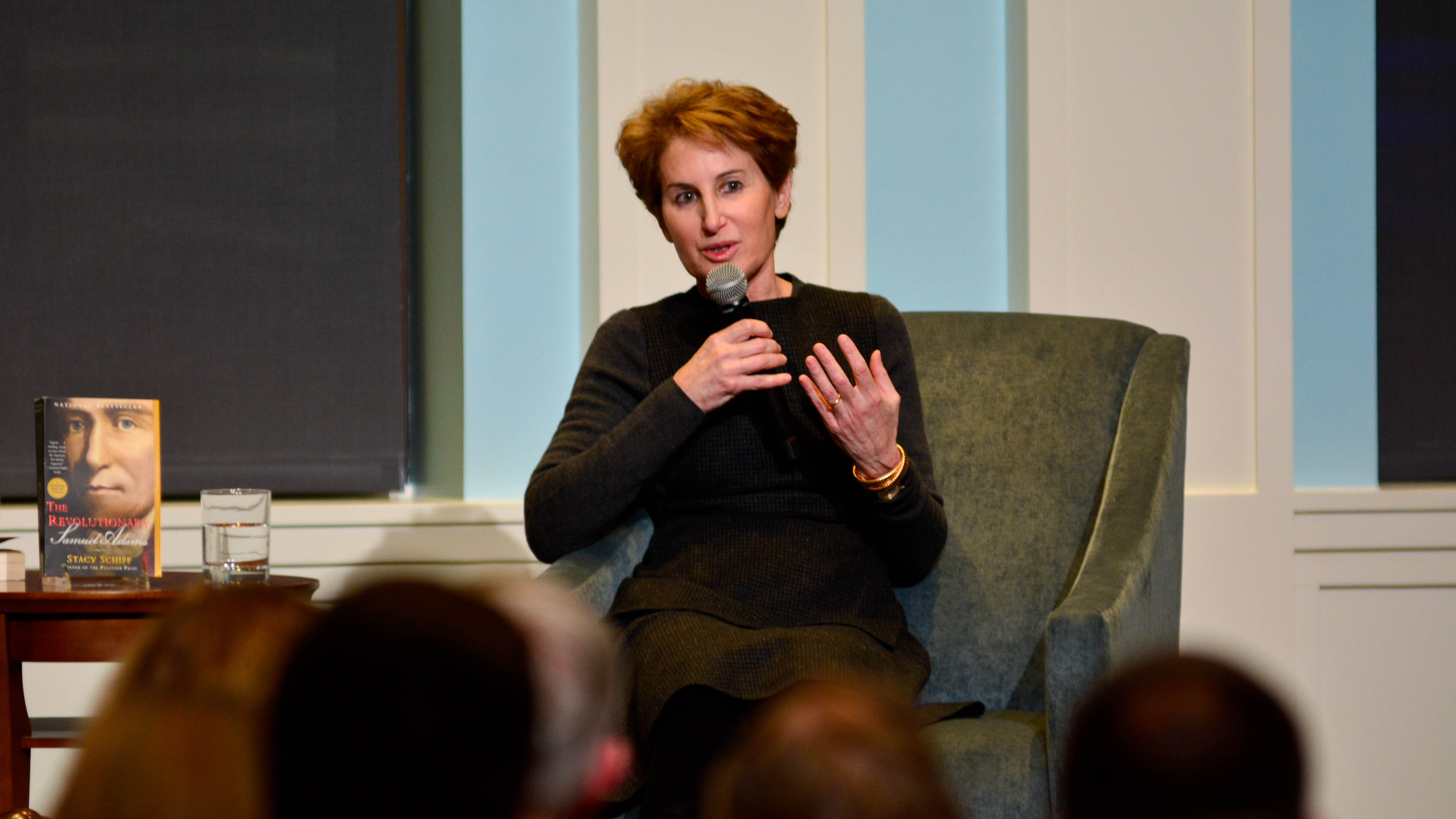 Stacy Schiff sits in a chair on stage in Liberty Hall wearing a black longsleeve dress and short brown hair discussing her book The Revolutionary.