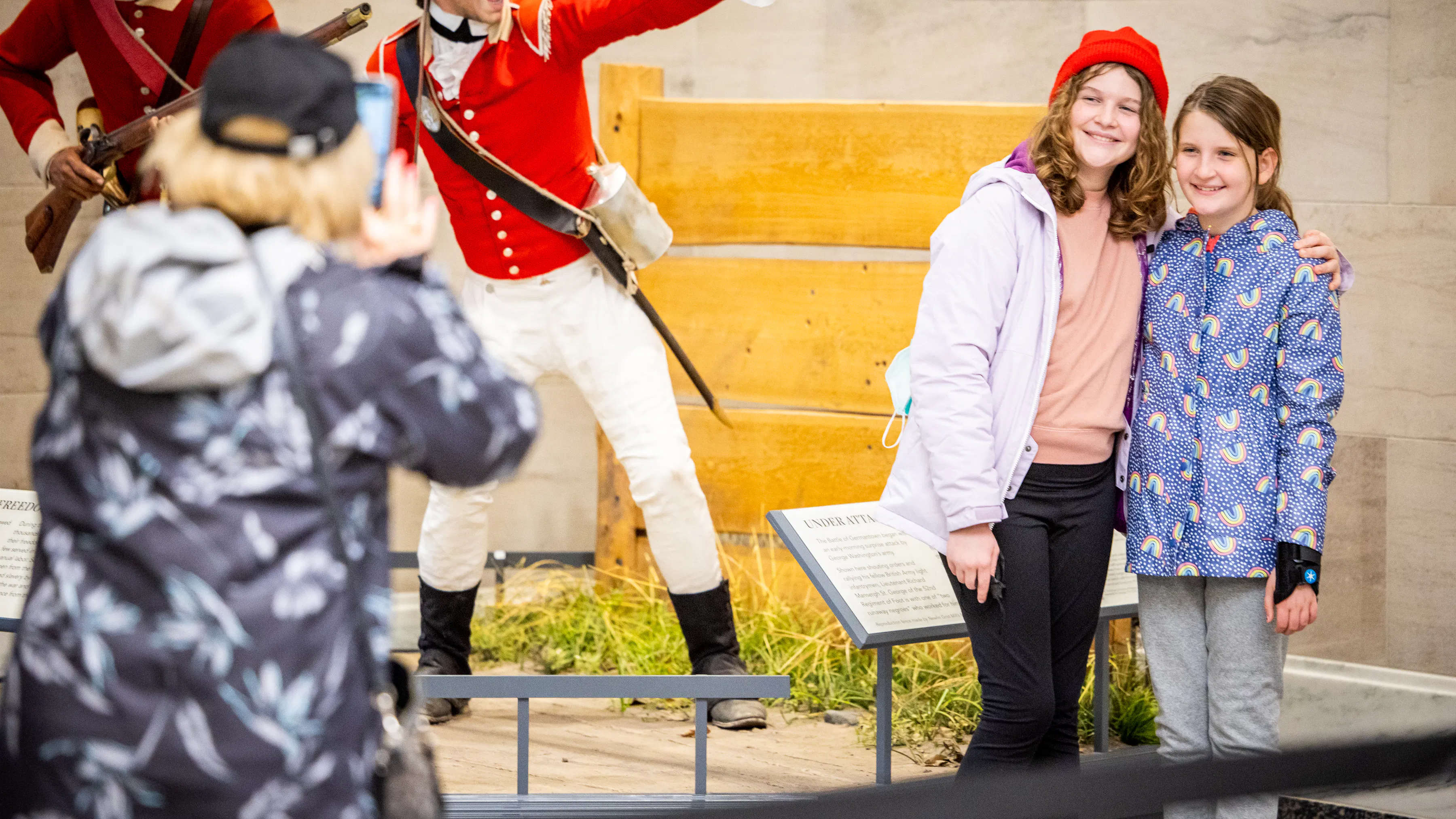 Two girls stand smiling posing for a picture in front of two figures