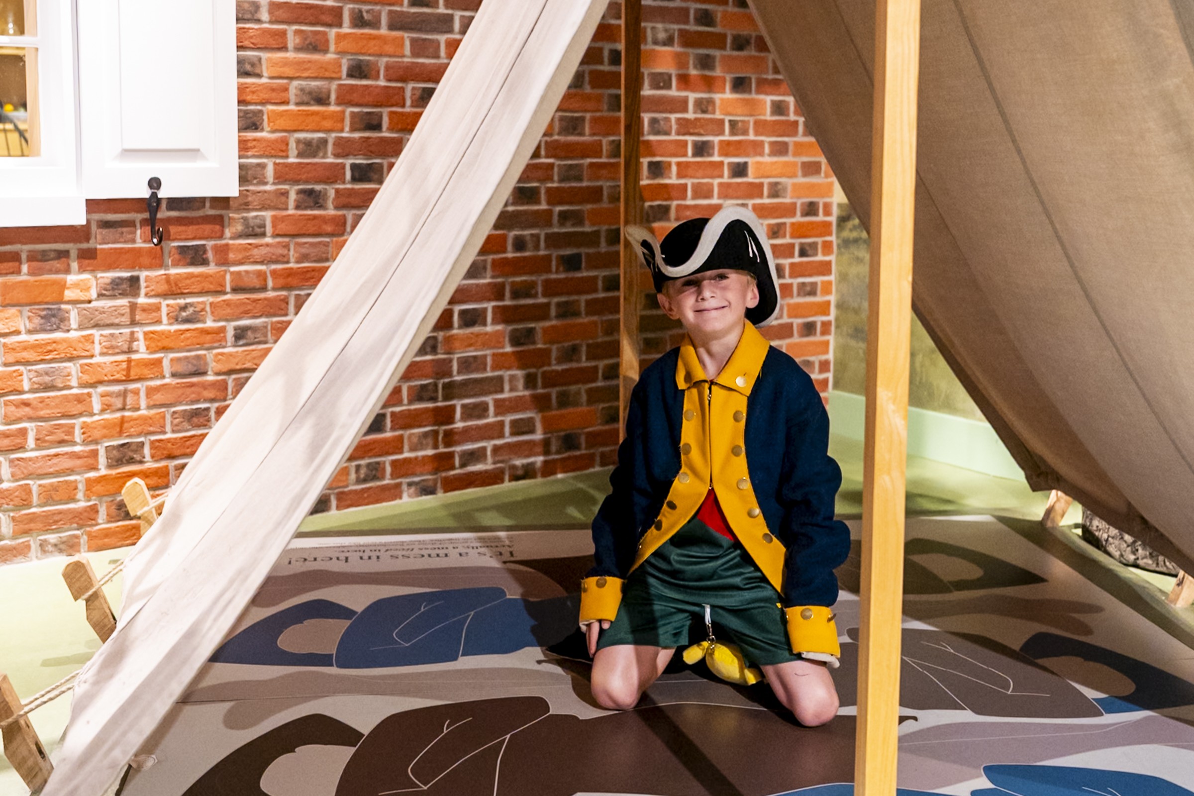A child in a Revolutionary War costume kneels inside a tent