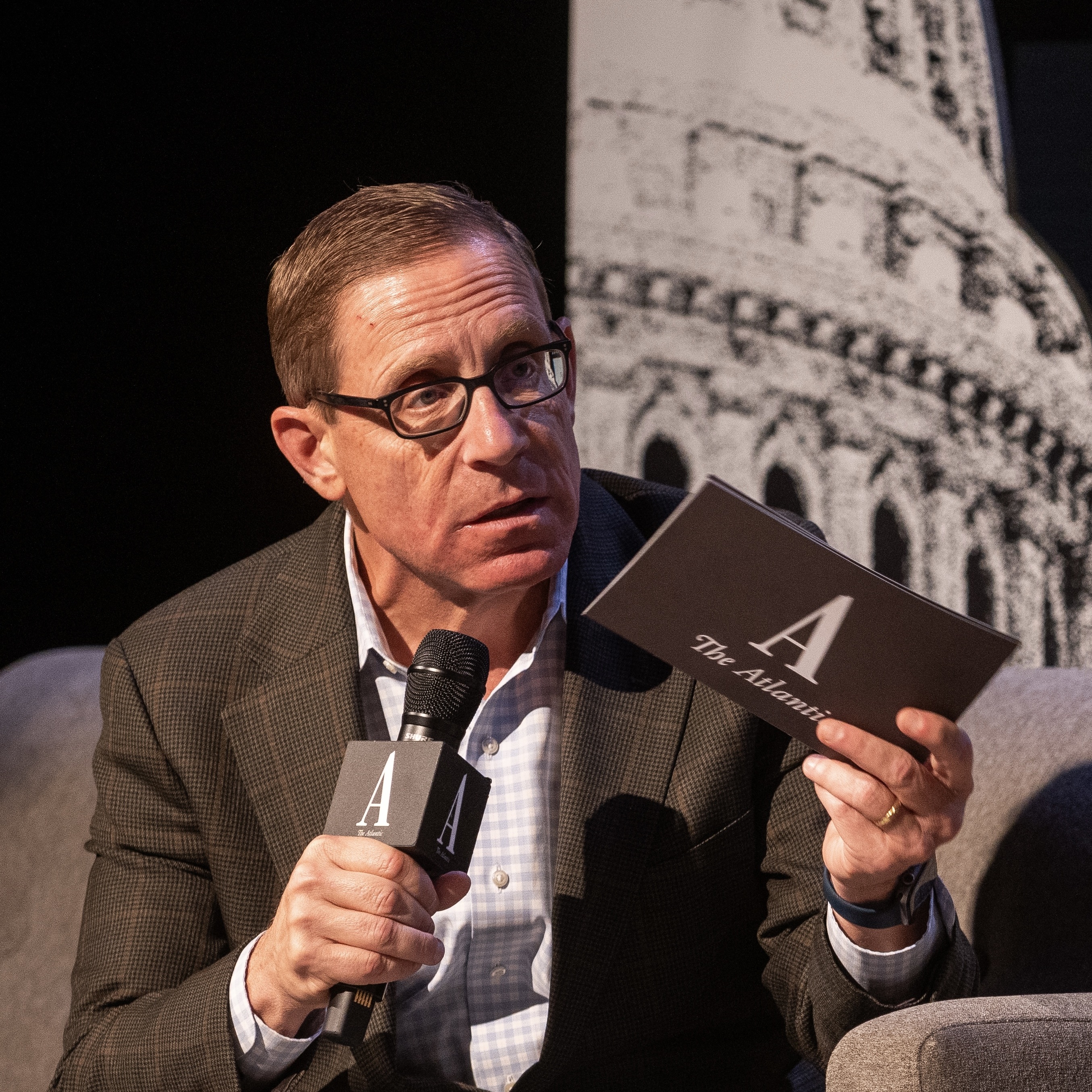 A man holding a microphone and a note card with The Atlantic's logo