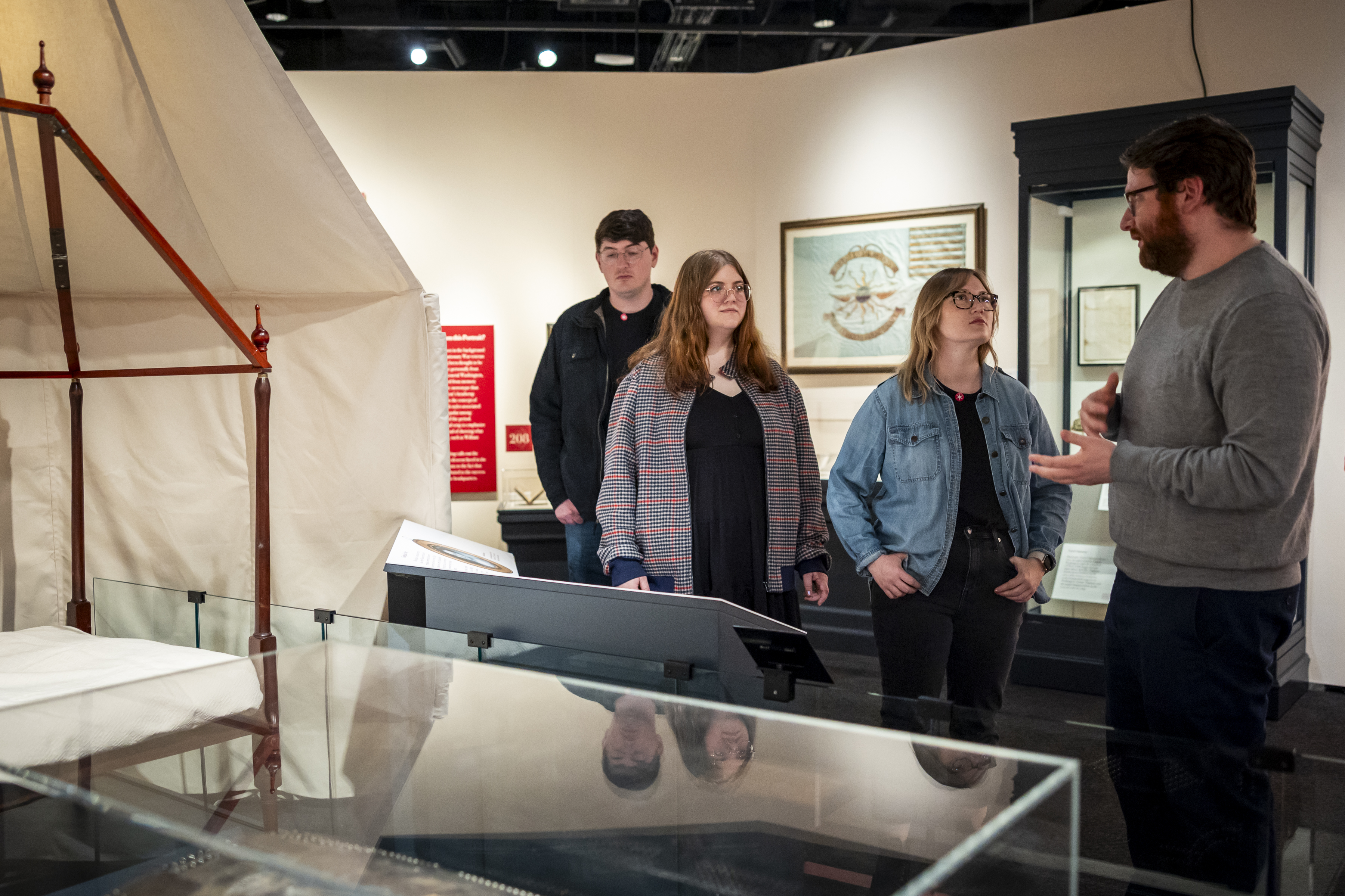 A Museum curator talks to three guests in Witness to Revolution at the partial recreation of one end of Washington's tent.