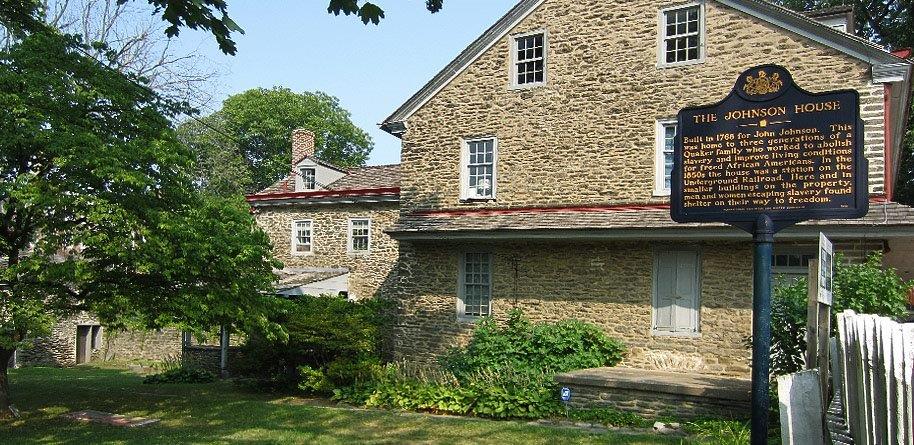 This image shows beige bricks on the side of the Johnson House and the blue historical marker to the right of the image.