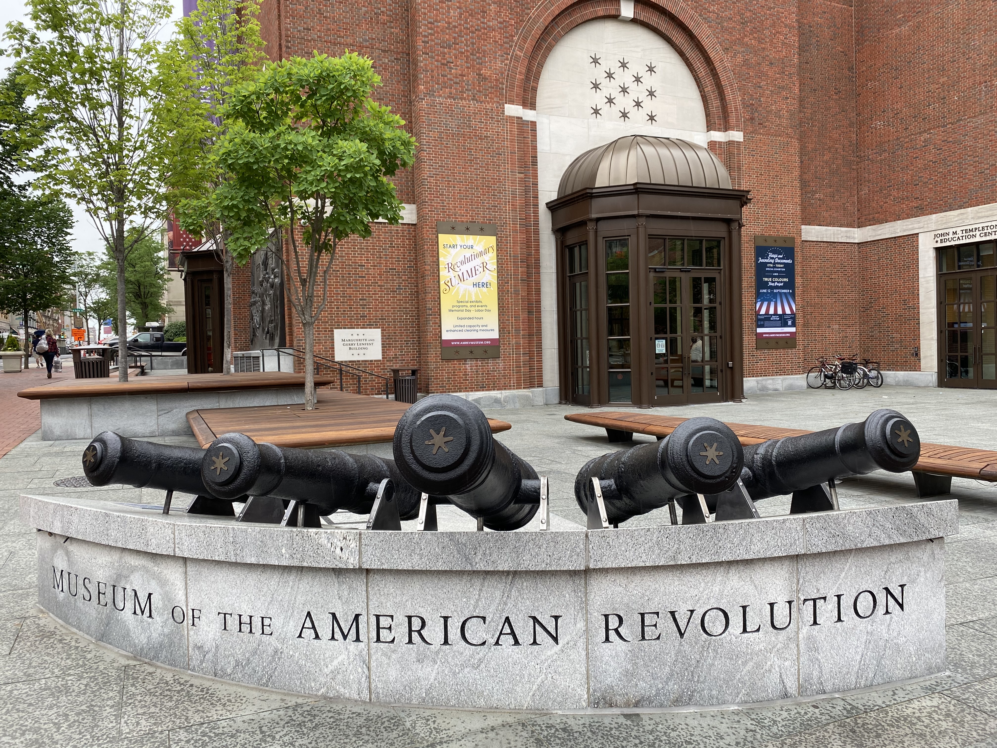 Five cannons on a stone base engraved with the words Museum of the American Revolution in front of a brick building