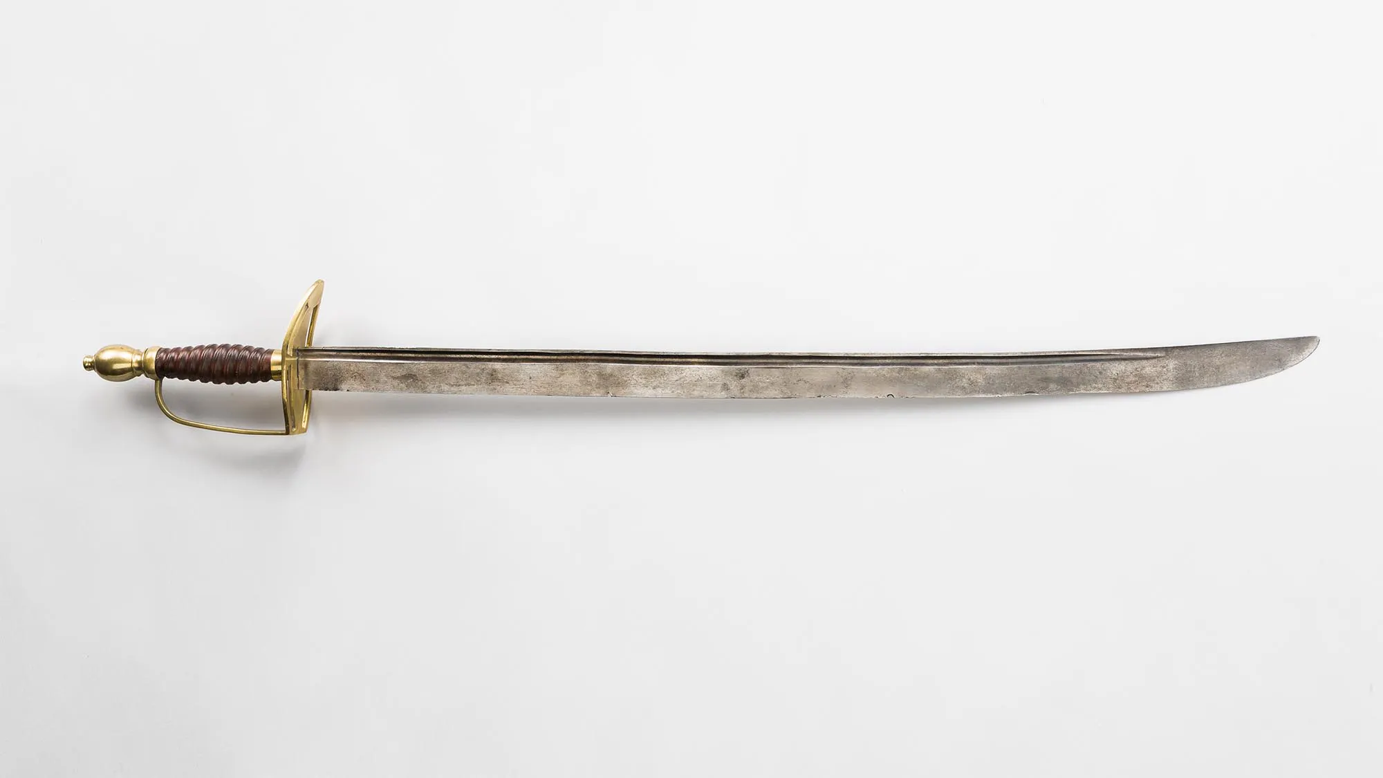 This image is of Benjamin Lincolns sword. The hilt is gold and is on the left side of the image, while the blade is pointing to the right of the image. The sword is resting against a white background.
