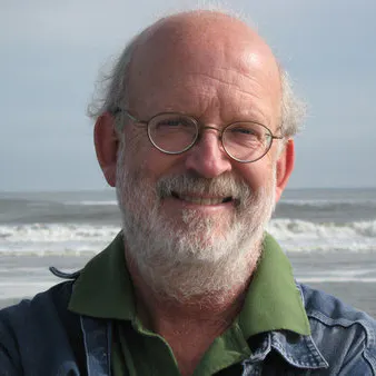 Tim McGrath headshot with white beard, glasses, and the ocean in the background.
