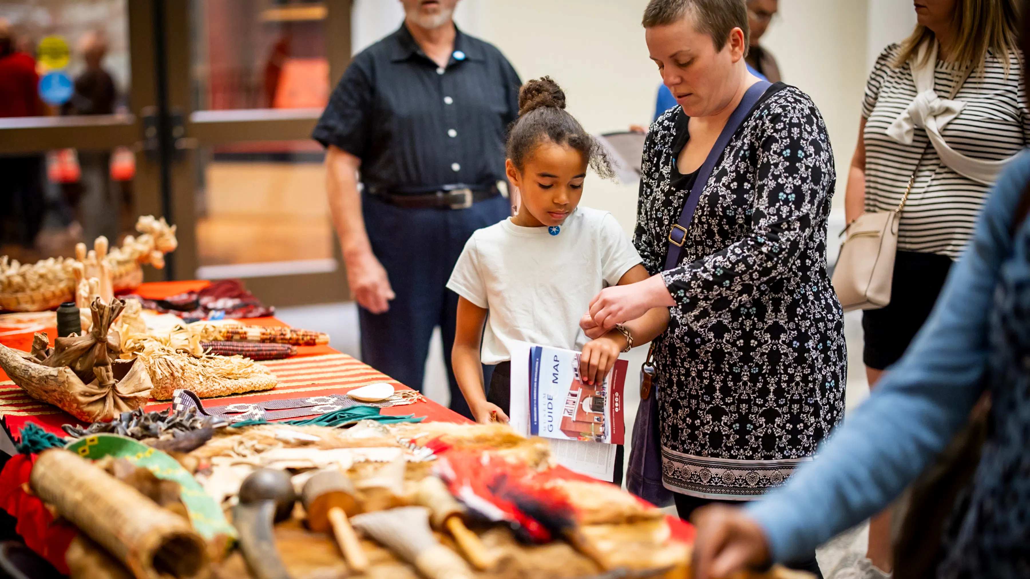 A woman and child stand in front of a table with Native American artifacts