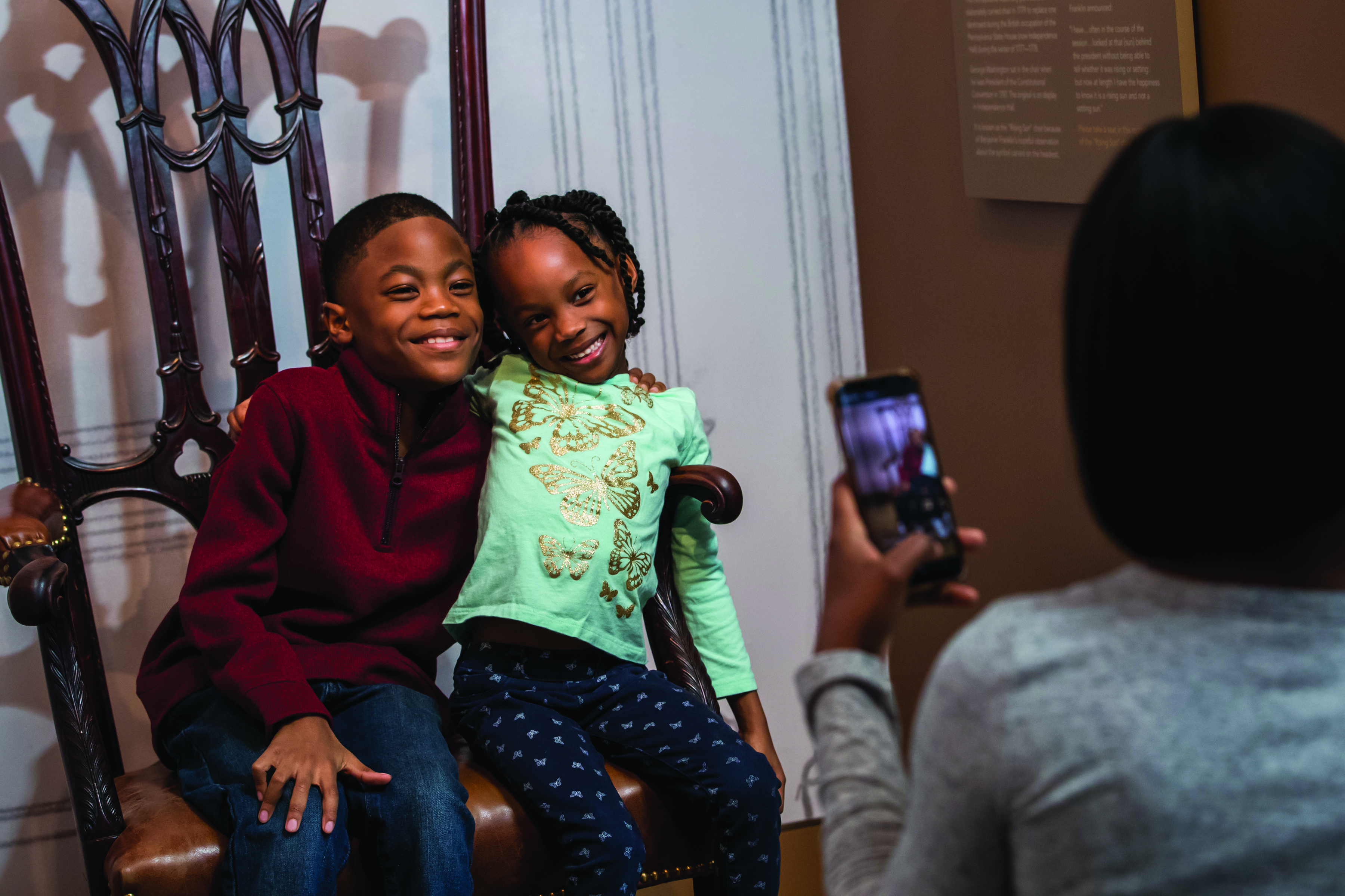 Two young visitors have their photo taken while sitting on the Rising Sun chair.