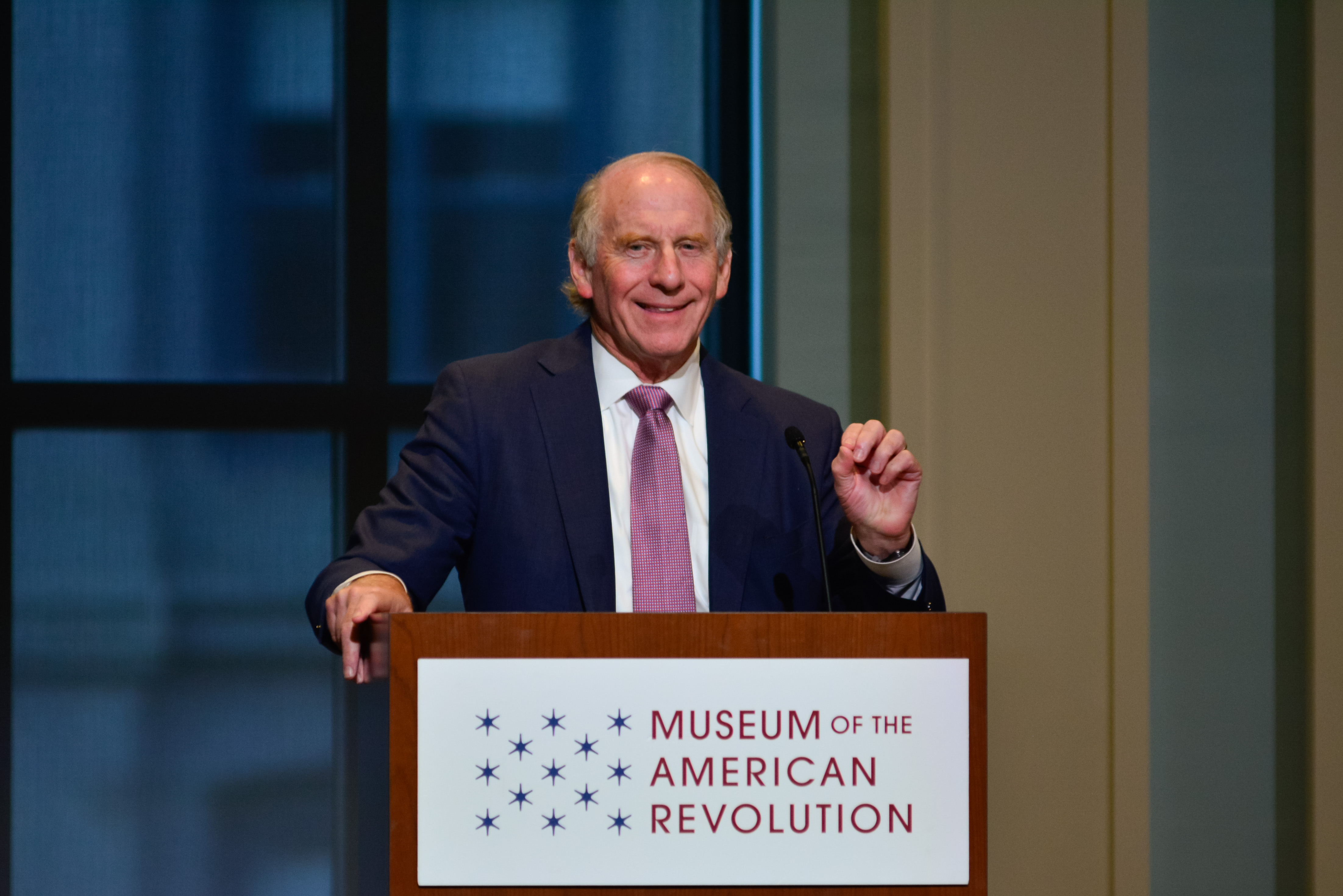 This image shows Dr. Richard Haass speaking at a podium with the Museum logo as he wears a dark blue suit and purple tie.
