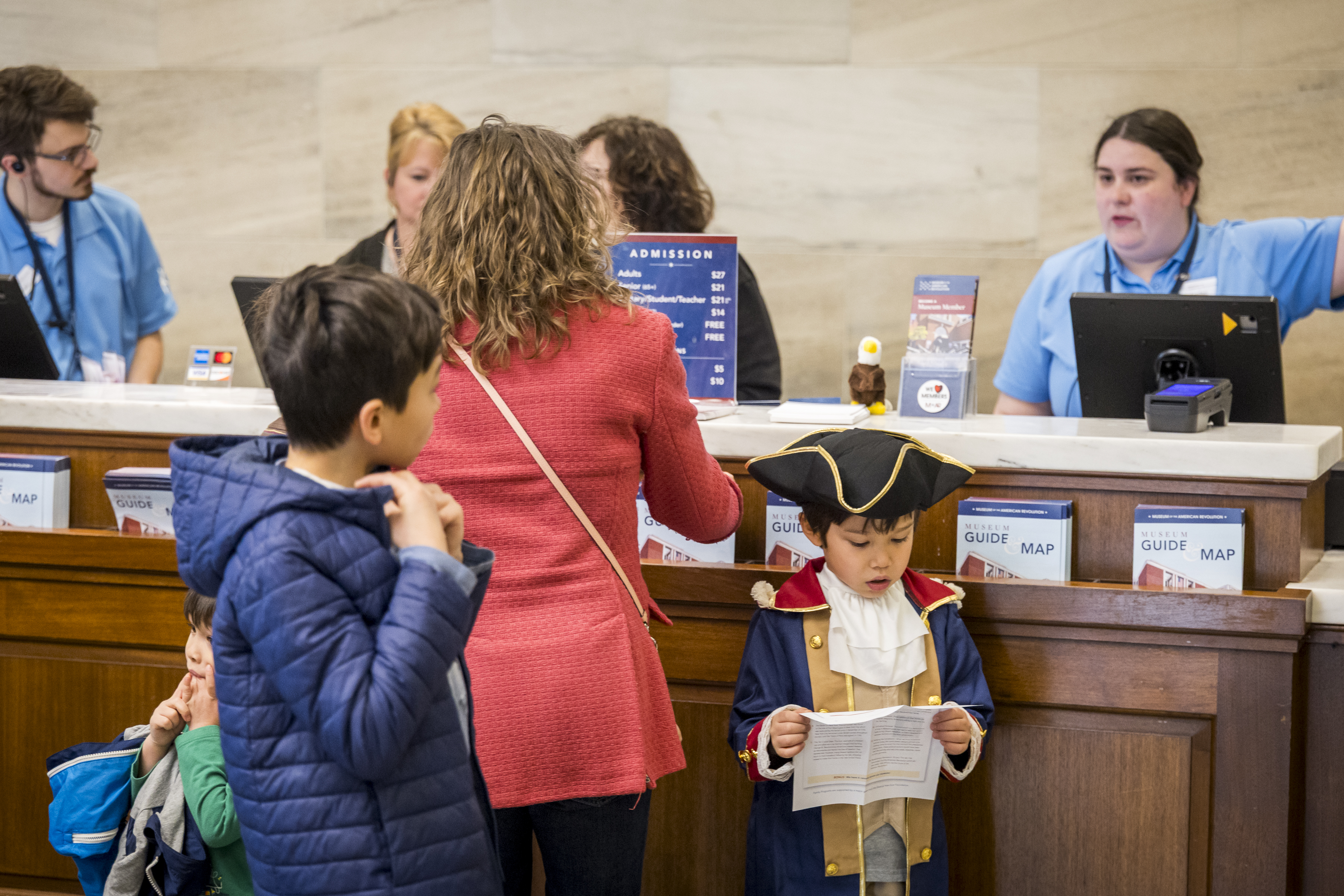 A woman and two children stand in front of a counter, where three people stand in light blue shirts