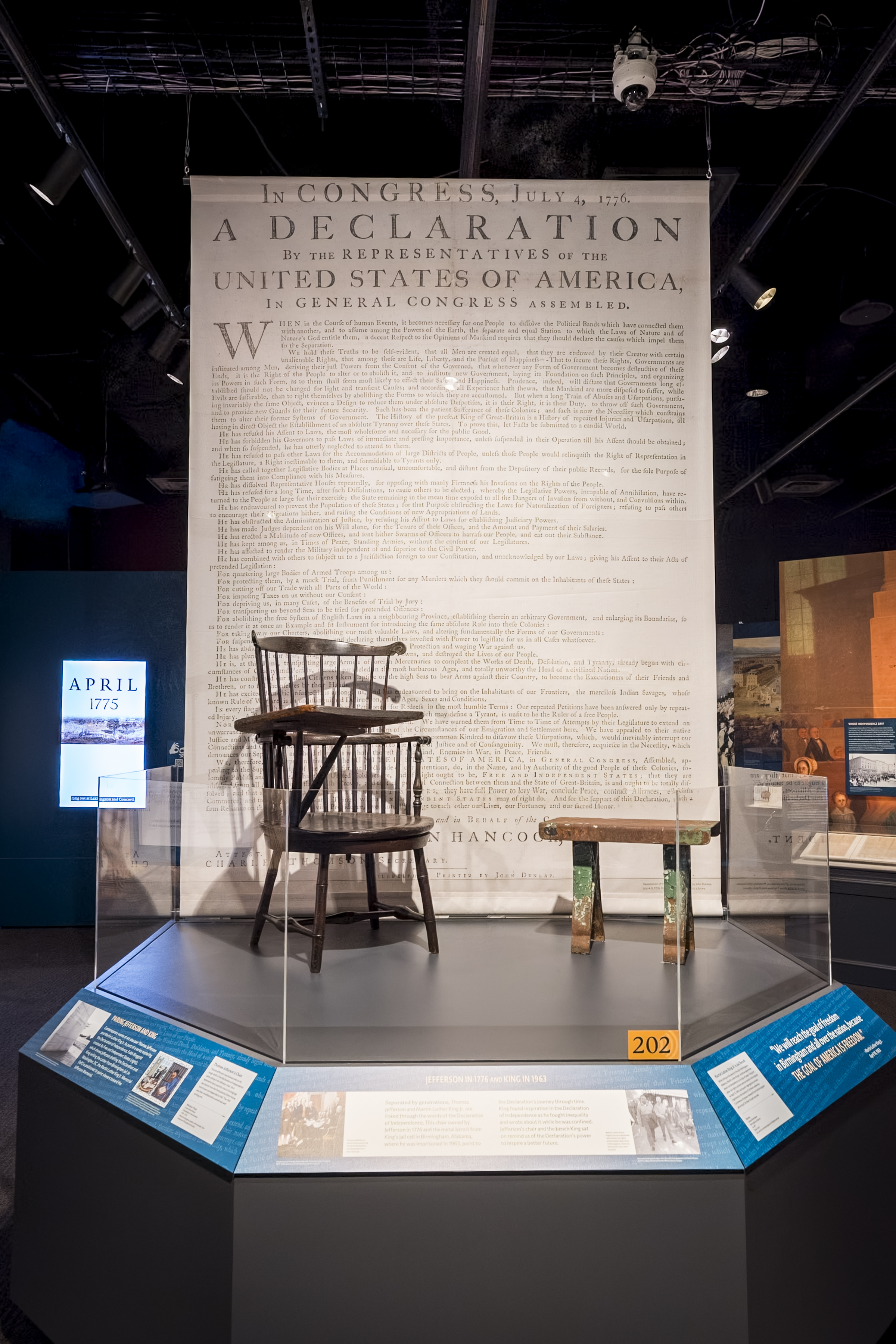 A chair and a bench on a platform in front of a large reproduction of the Declaration of Independence