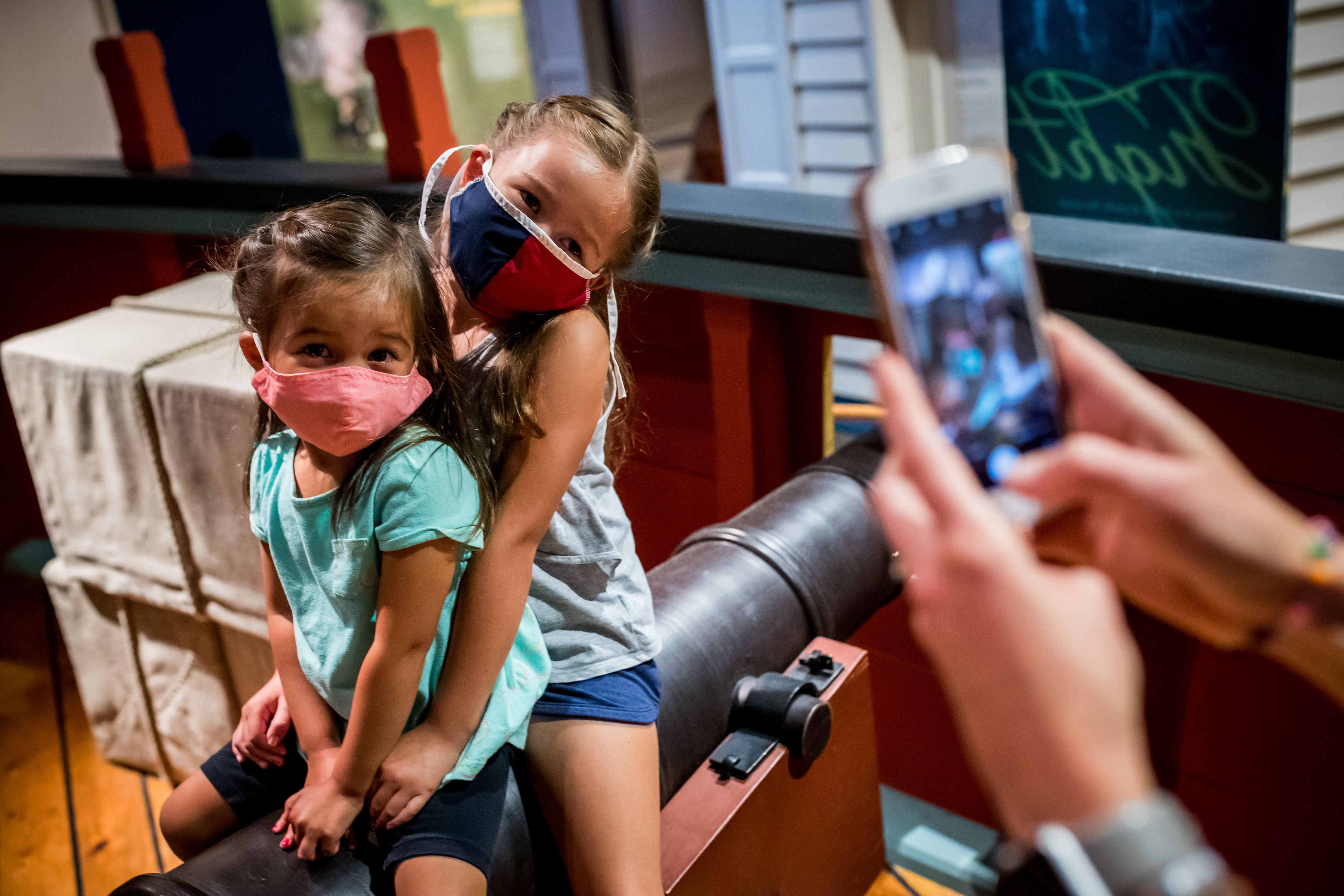 A mother takes a picture of her two young daughters, all wearing masks, on one of the cannons of the Privateer Ship in the galleries.