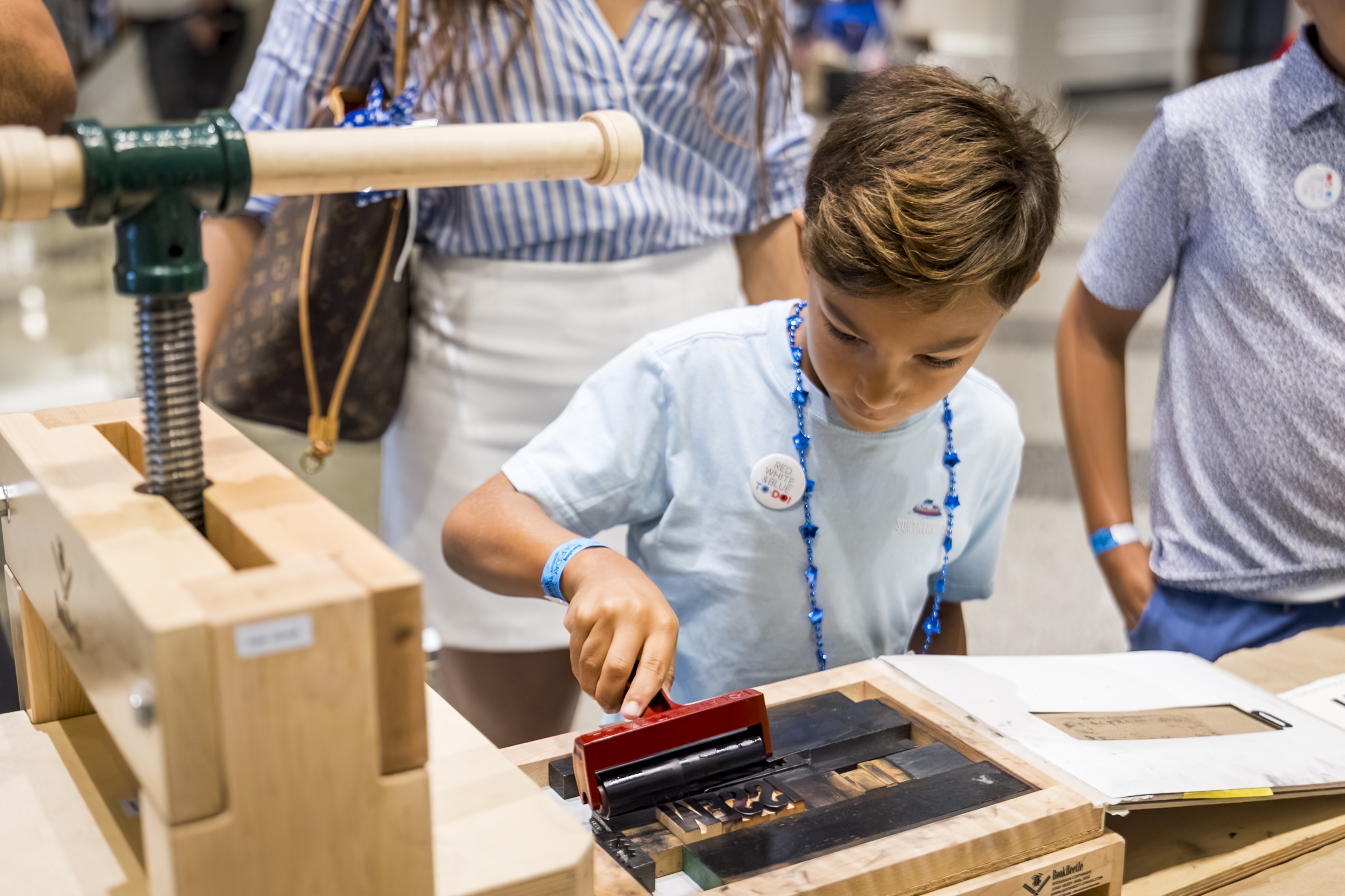 A child uses an ink roller on a wooden printing press