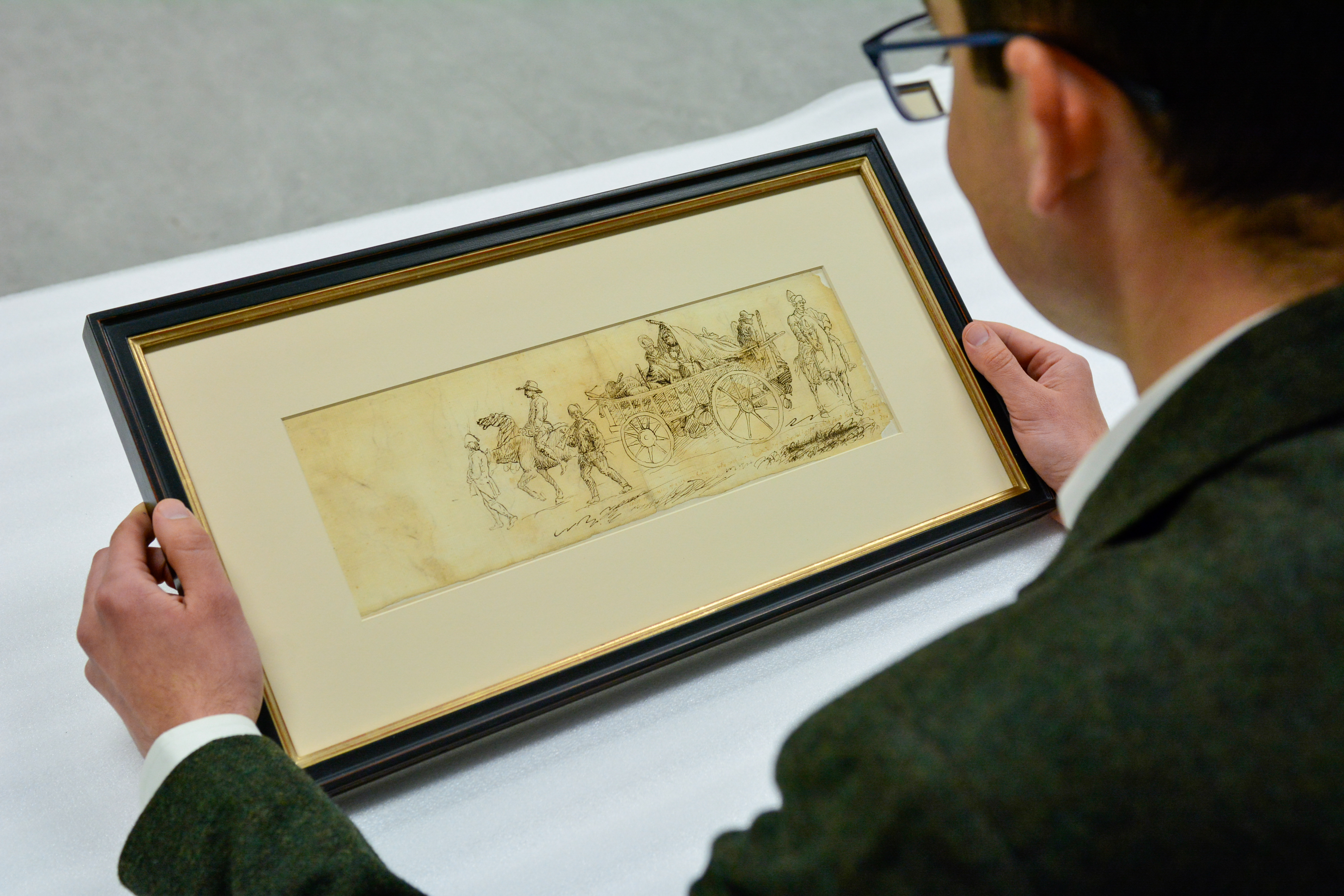 Curator Matthew Skic holds and views the framed eyewitness sketch of the North Carolina Brigade and women camp followers marching through Philadelphia.