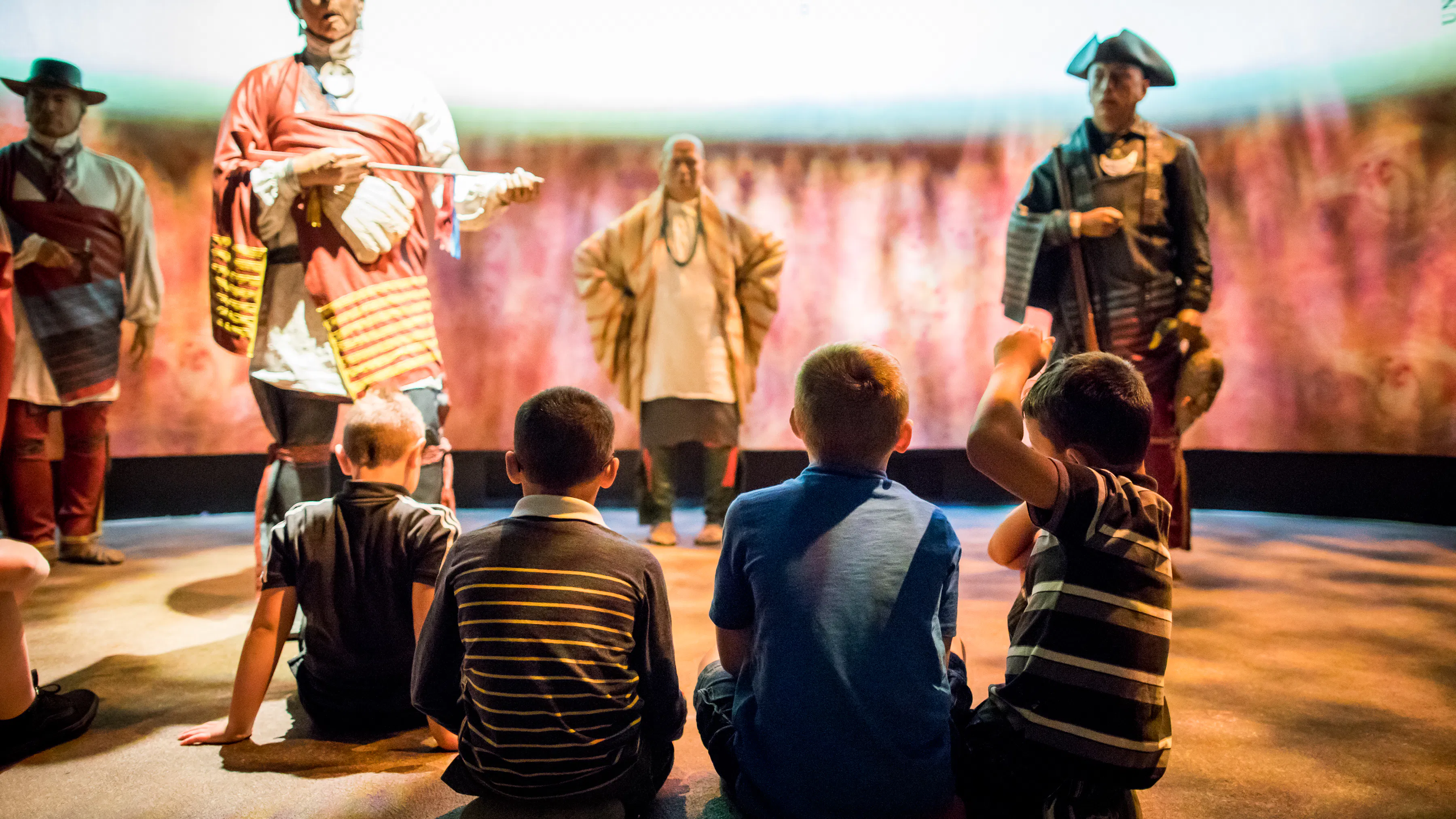 Four young boys seated in front of three Native American figures in the Museum's Oneida Nation Gallery.