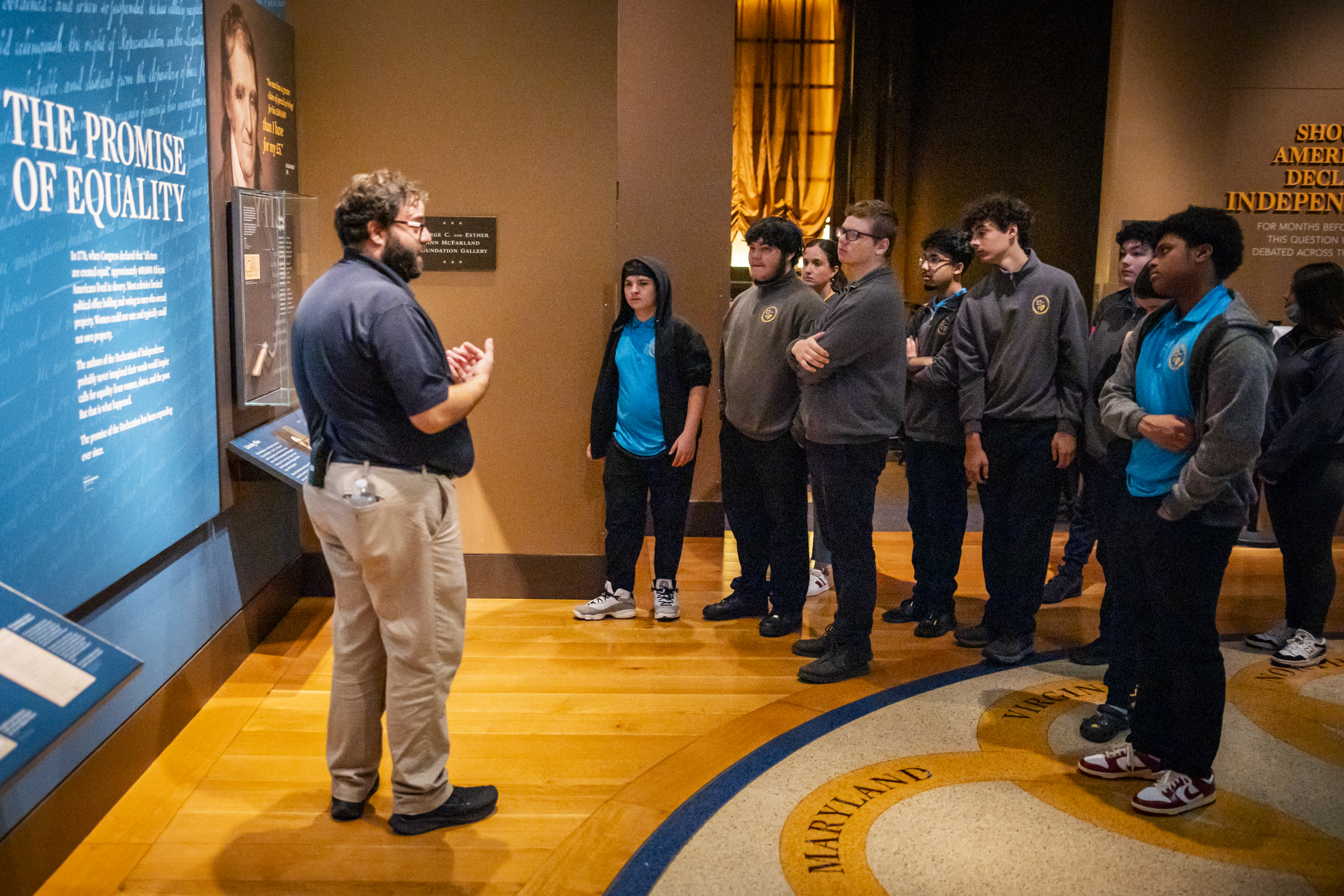 A Museum educator speaks to a school group in a gallery discussing the promise of equality.