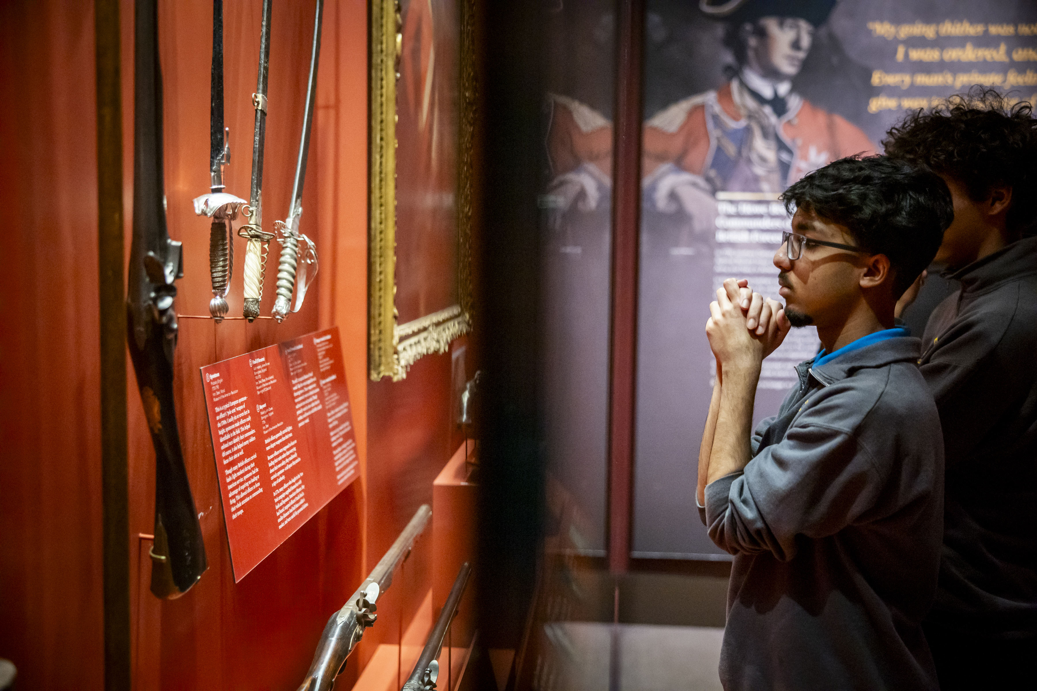 A school student on a tour views swords in a gallery discussing battles in New York.