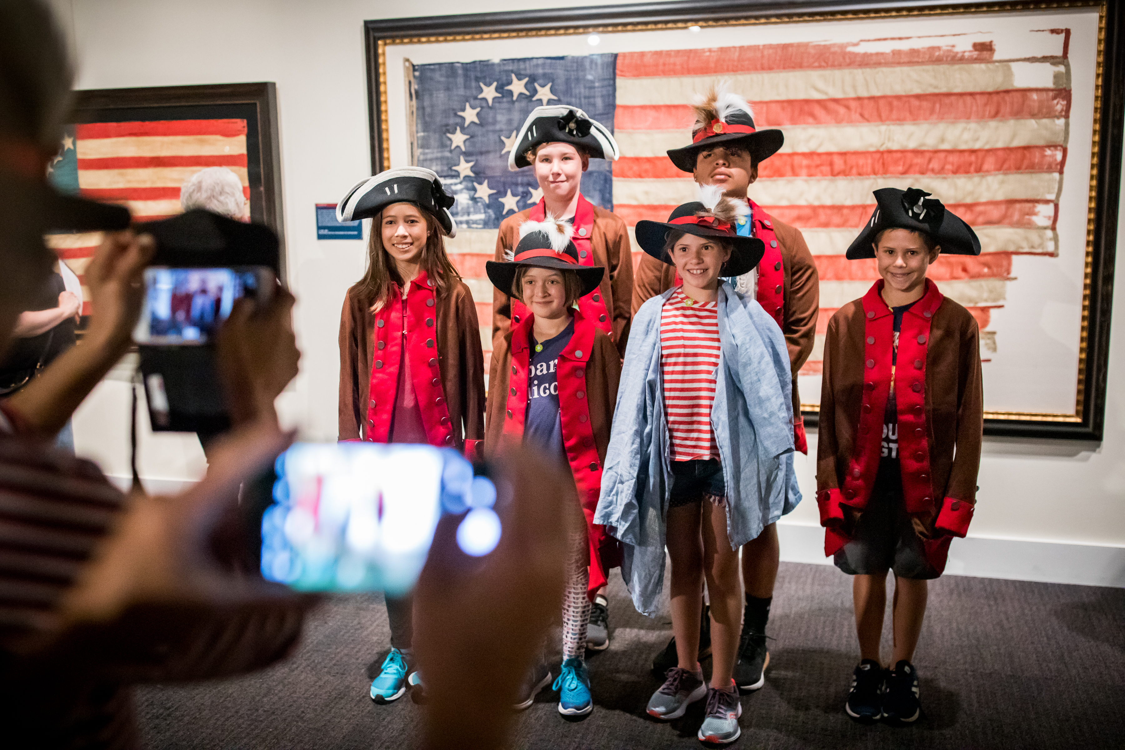 Six adolescents, wearing Revolutionary-era costumes, pose for a picture in front of a 13-star flag, which was part of the Museum's summer 2019 exhibition, A New Constellation.