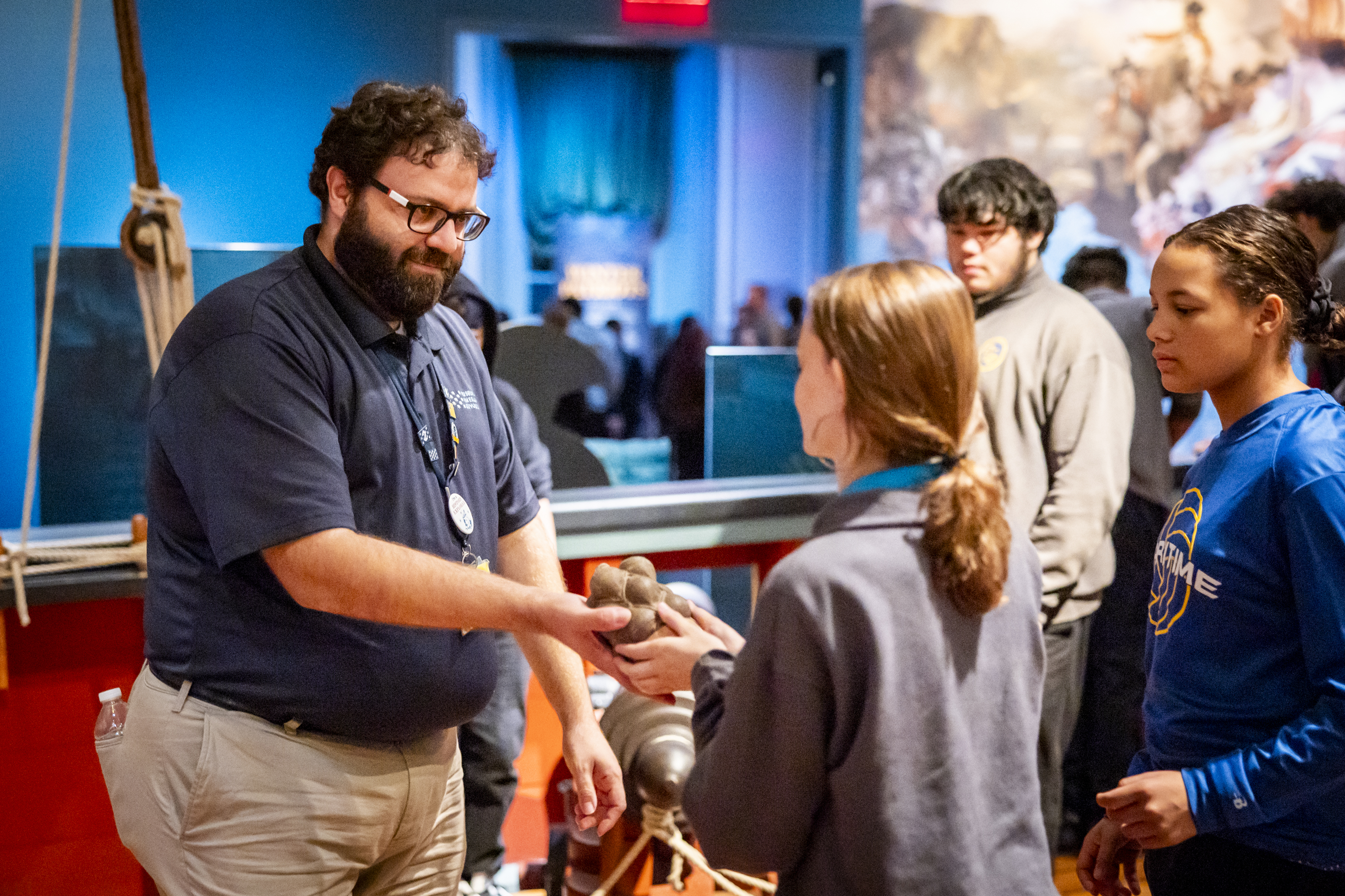 Museum educator wearing navy blue shirt holds grapeshot for young student