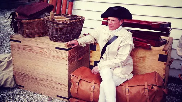 A costumed interpreter sitting on two stacked leather portmanteaux.