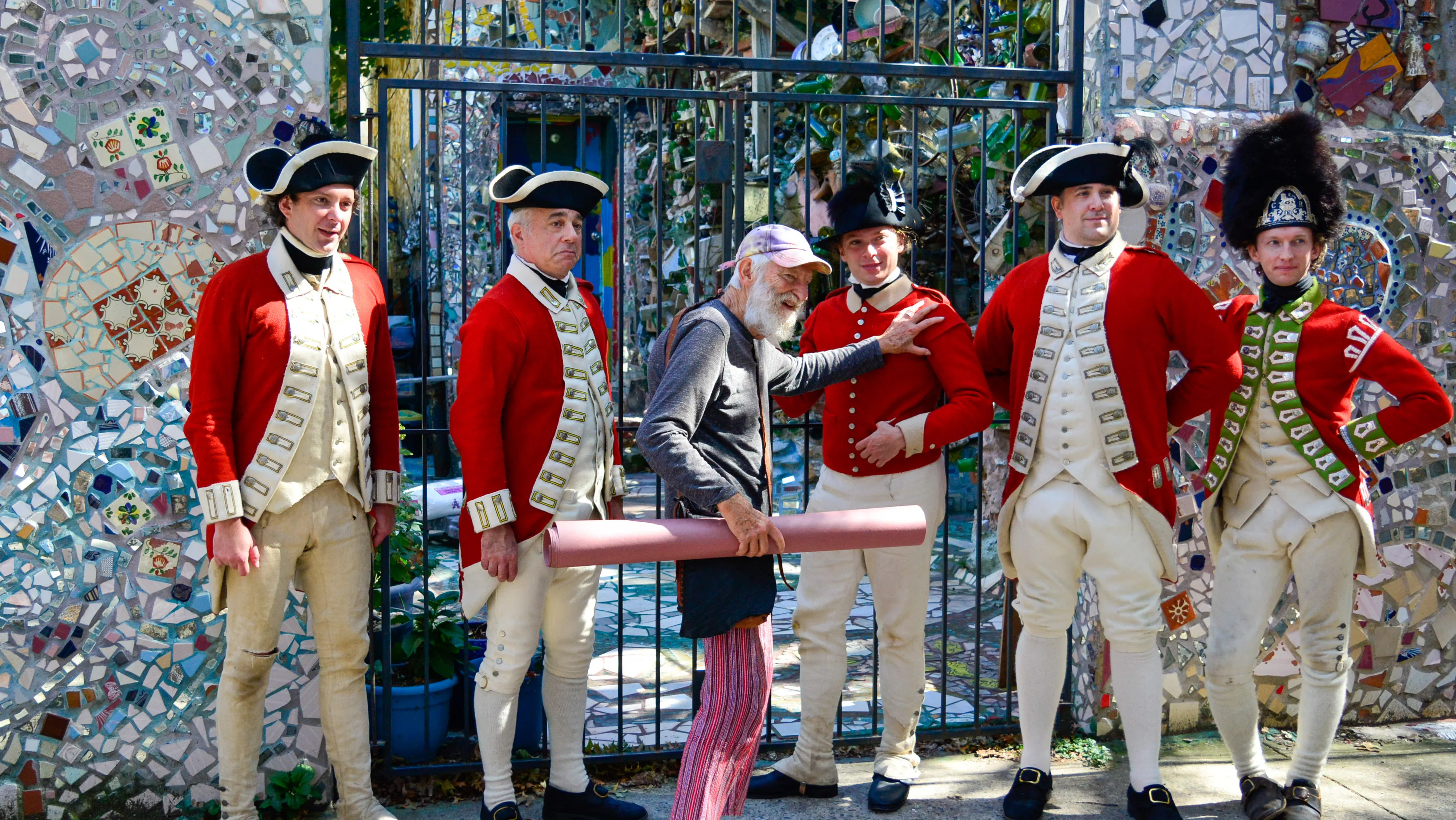A white man poses with five men in 18th century British uniforms