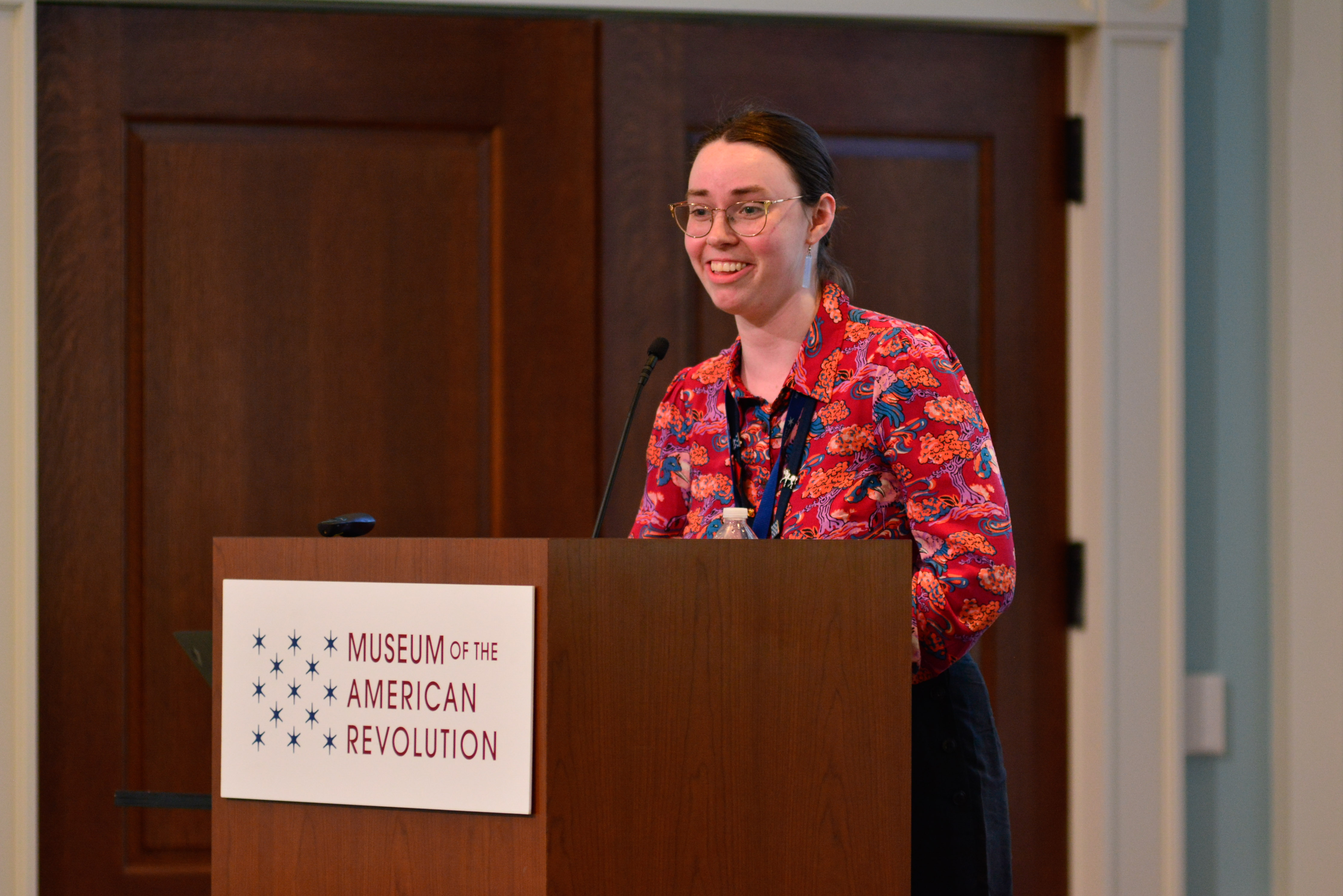 Clare McCabe discusses the Davenport baby booties at the Conference on Collecting the American Revolution while standing at a podium with the Museum logo on the front.