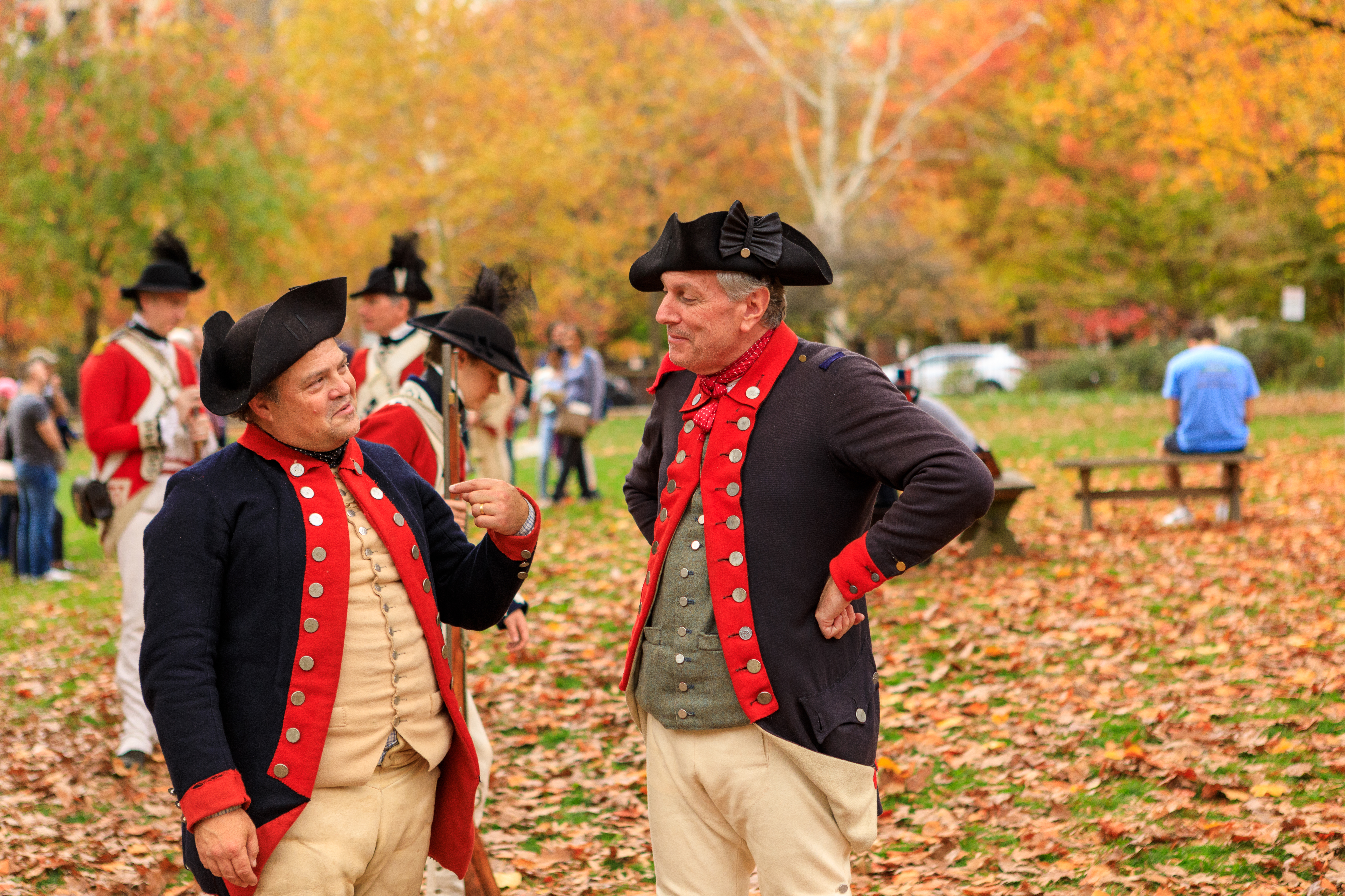 Two costumed interpreters stand in front of fall trees