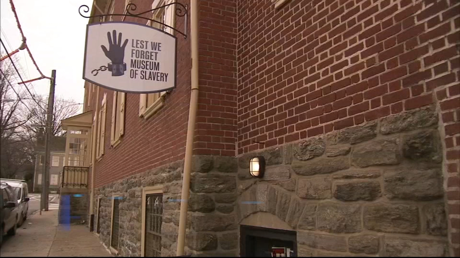 This image shows the brick facade and white sign of the Lest We Forget Slavery Museum in Germantown.