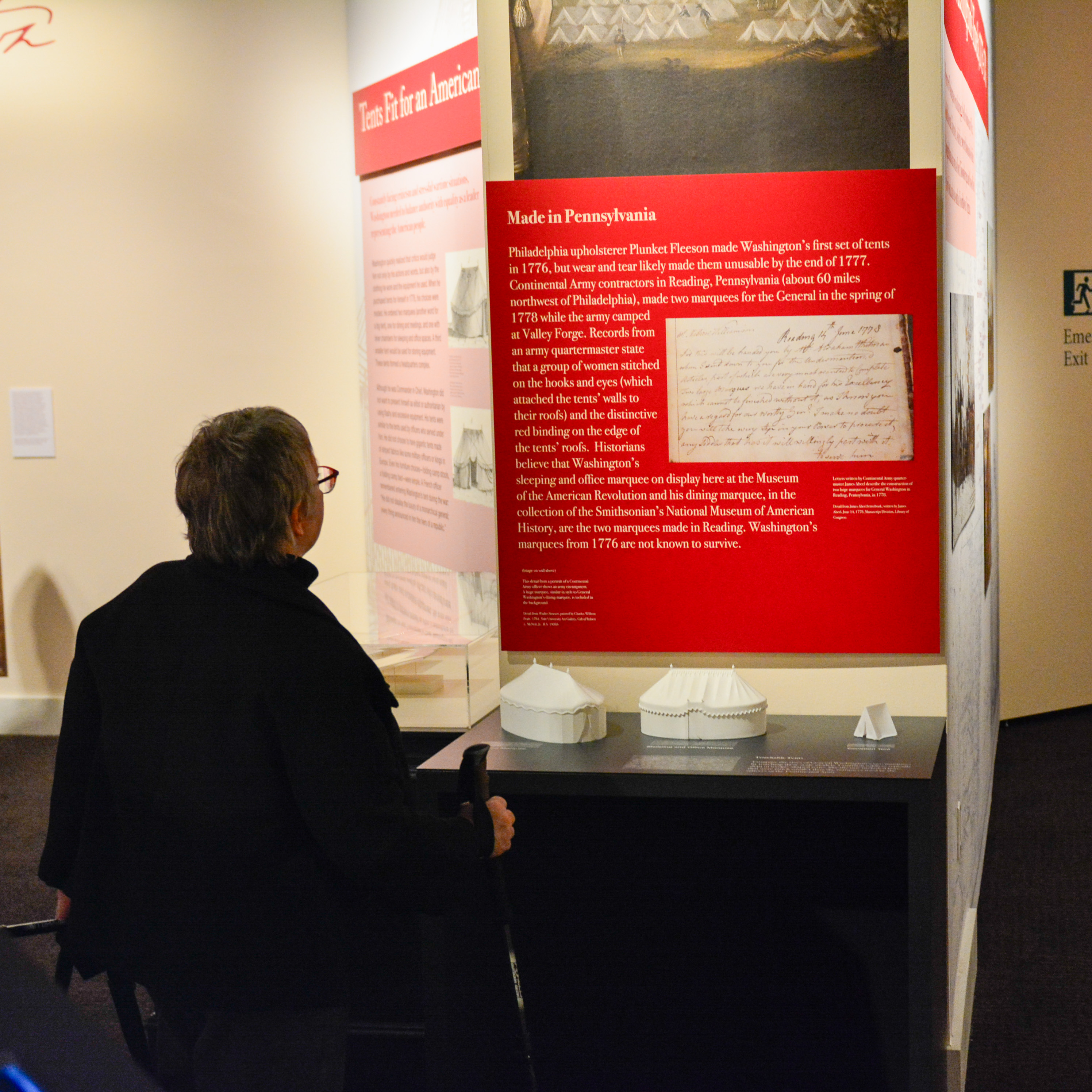 A guest reads a wall panel above the 3D-printed tactile versions of George Washington's tents in Witness to Revolution.