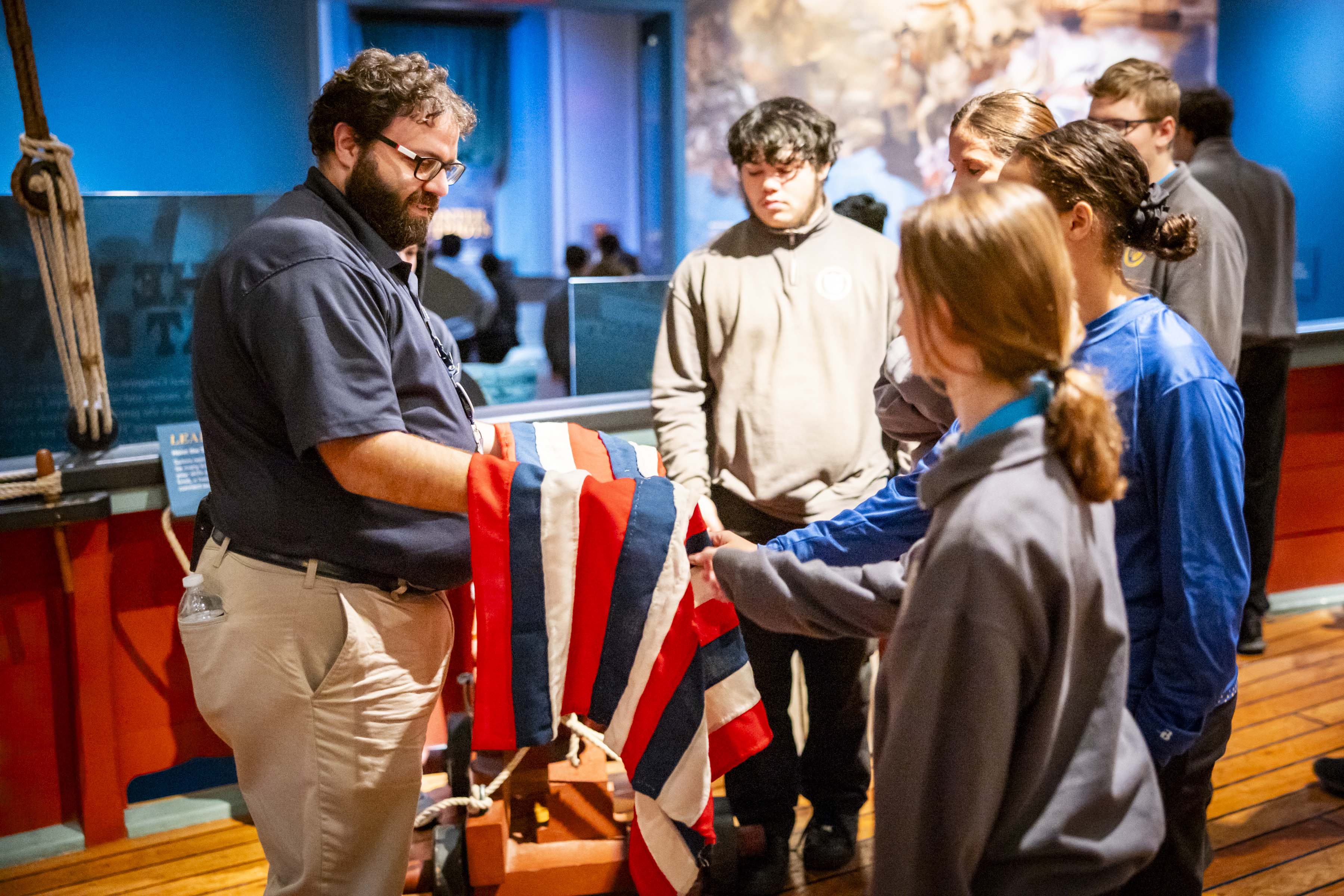 A Museum educator shows a replica flag to a group of school students aboard the sloop in the Museum's core exhibition.