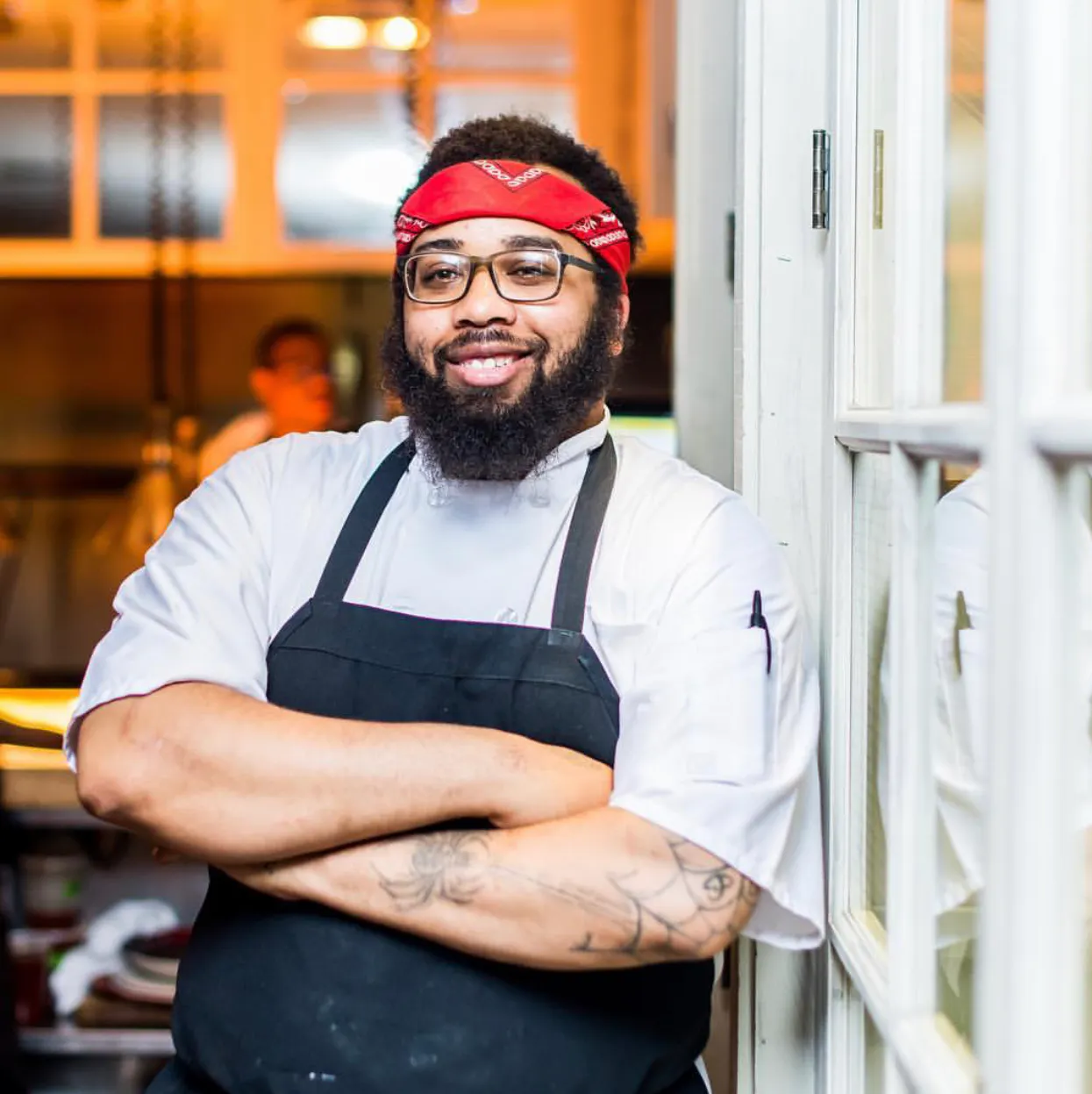 Portrait of Chef Kurt Evans wearing a red bandana headband, white chef's shirt and black apron.