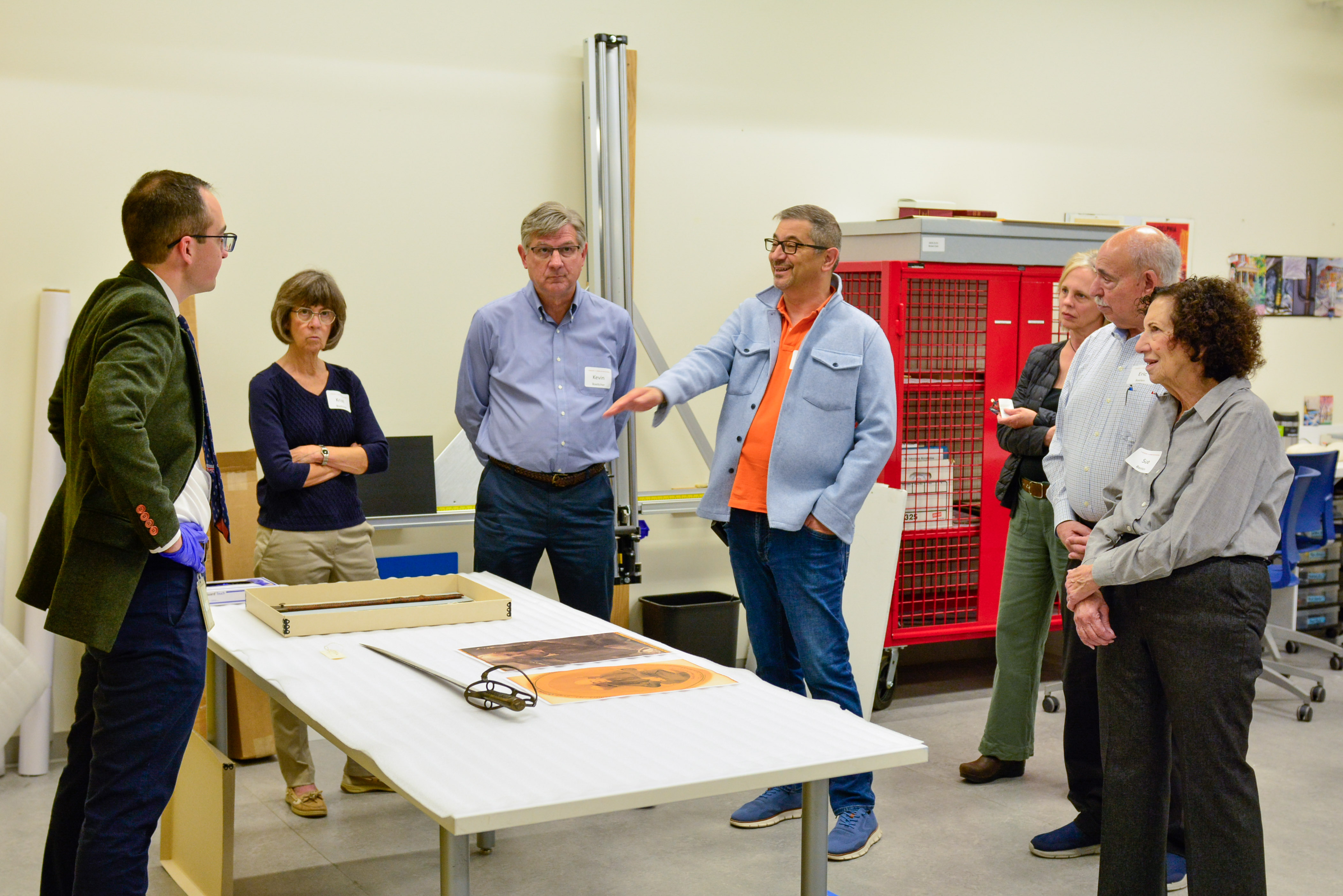 People standing around a white table looking at antique objects