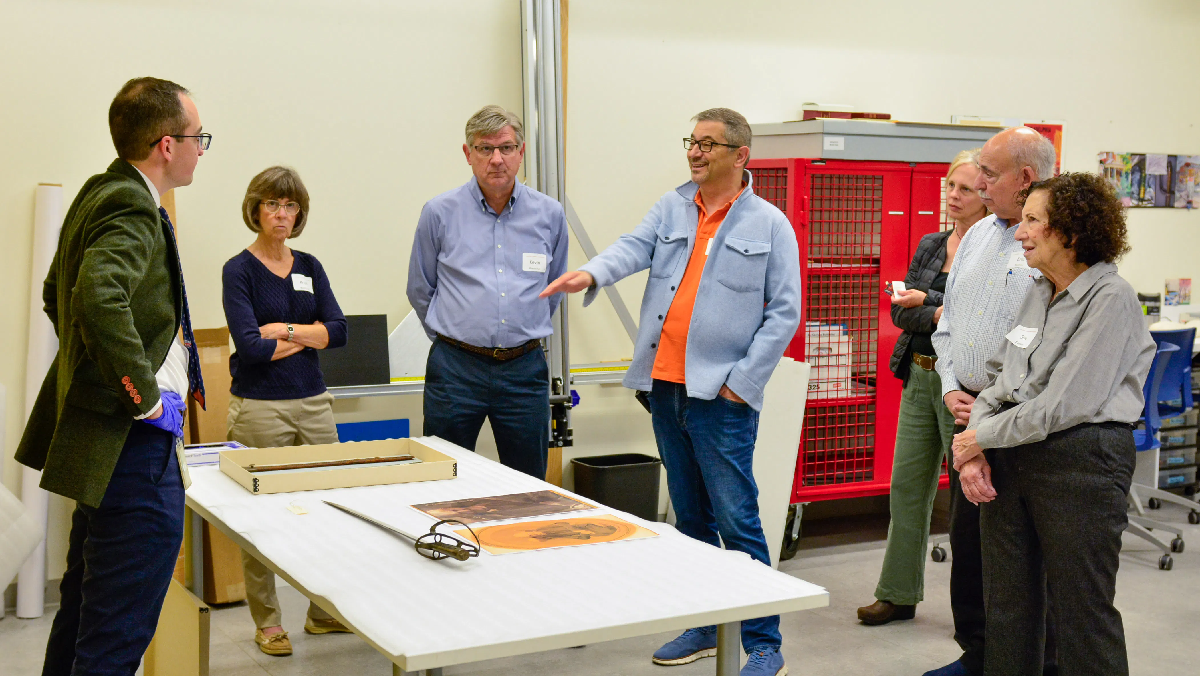 People standing around a white table looking at antique objects
