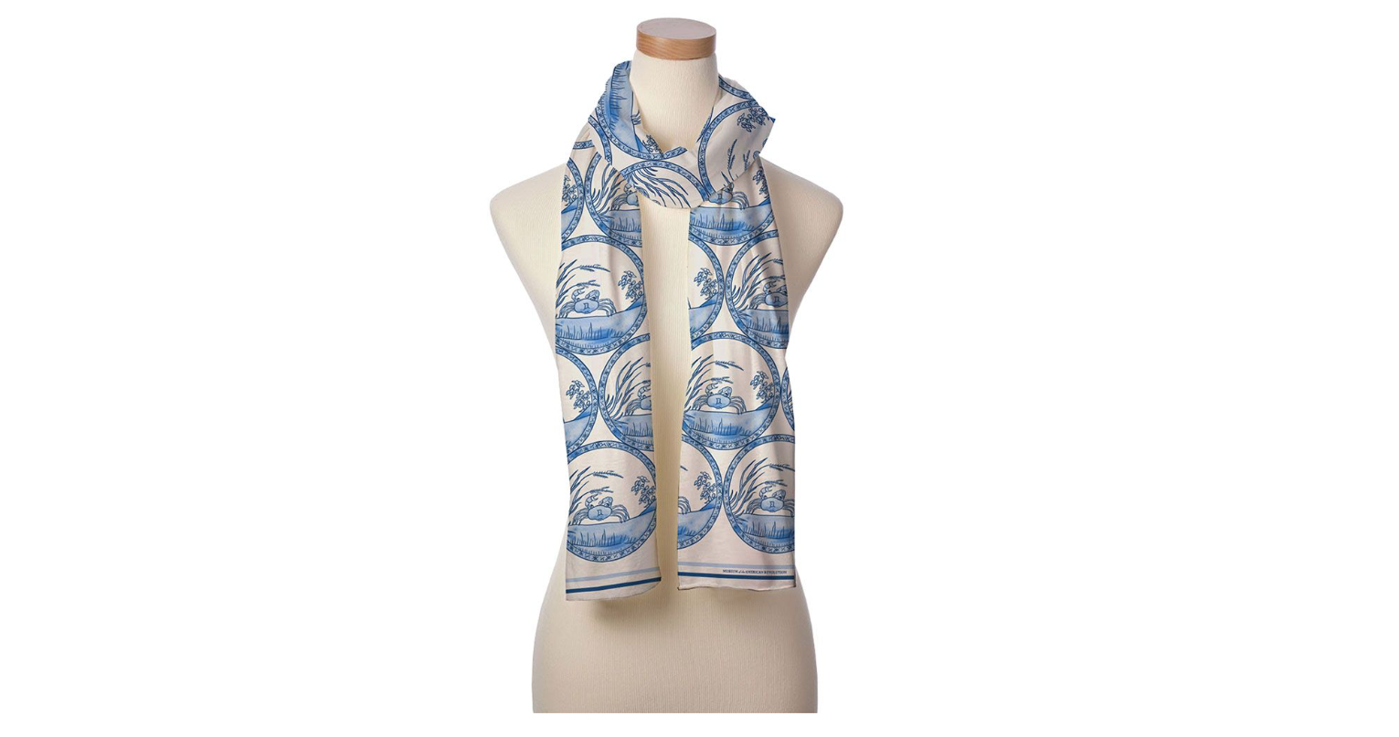 This image shows a mannequin with a white and blue scarf draped around its neck with the pattern of a blue crab on it.