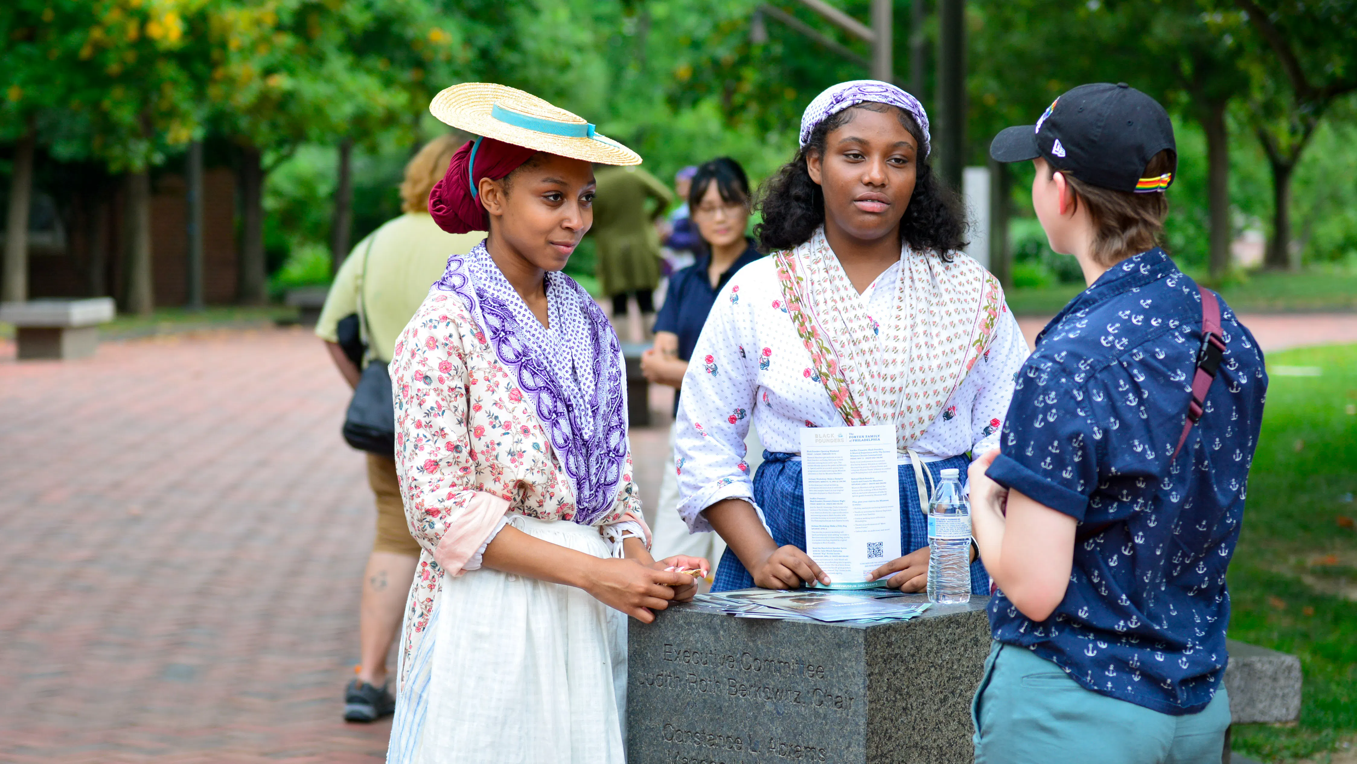 Two women in 18th century clothing speaking with person in modern clothing