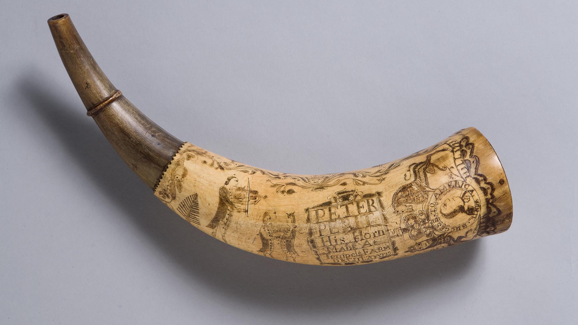 This image shows the powder horn of Peter Perit. The horn has illustrations of a king and his horse, as well as a violinist and two figures dancing.