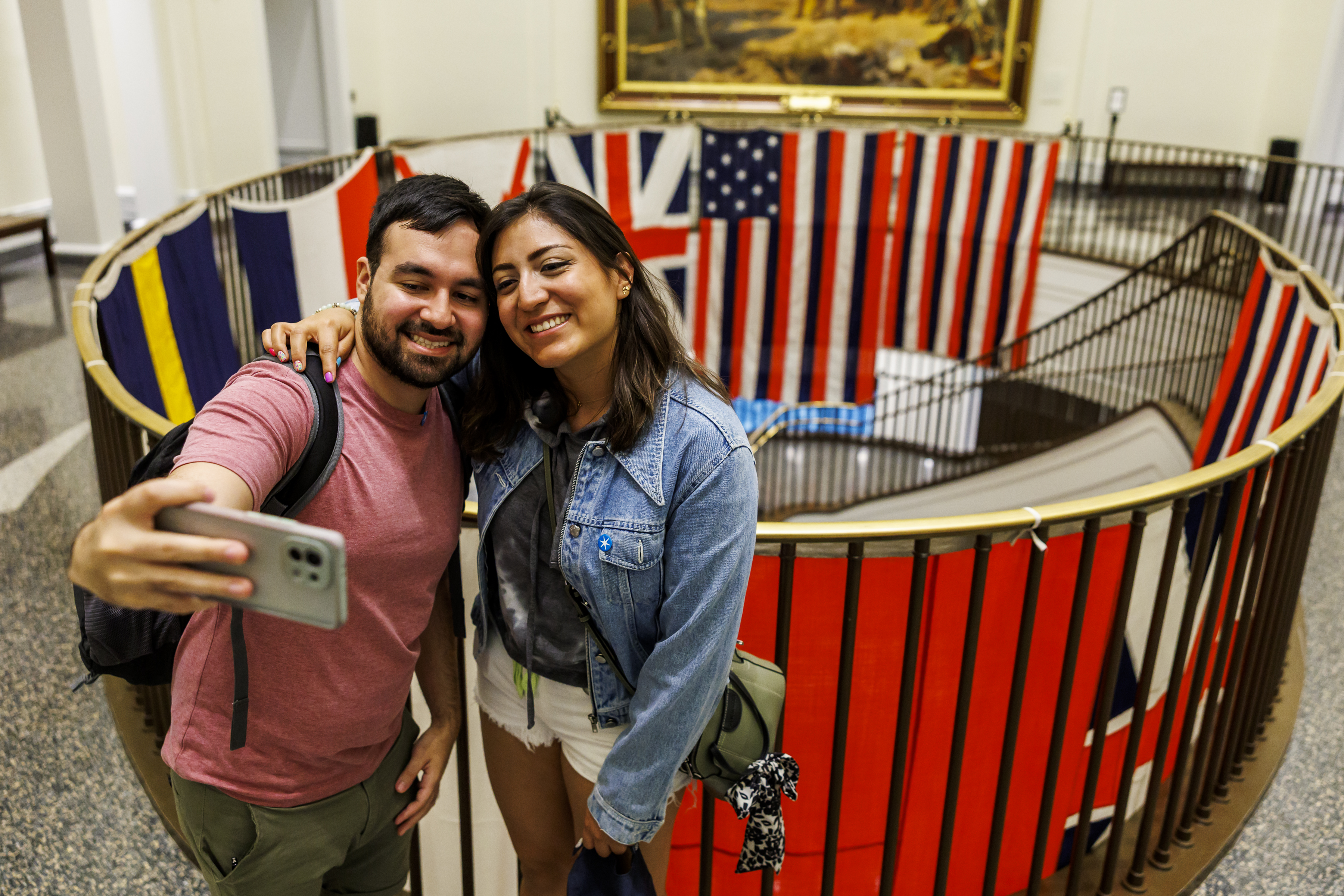 Two people take a selfie in front of colorful flags hanging in a stairwell