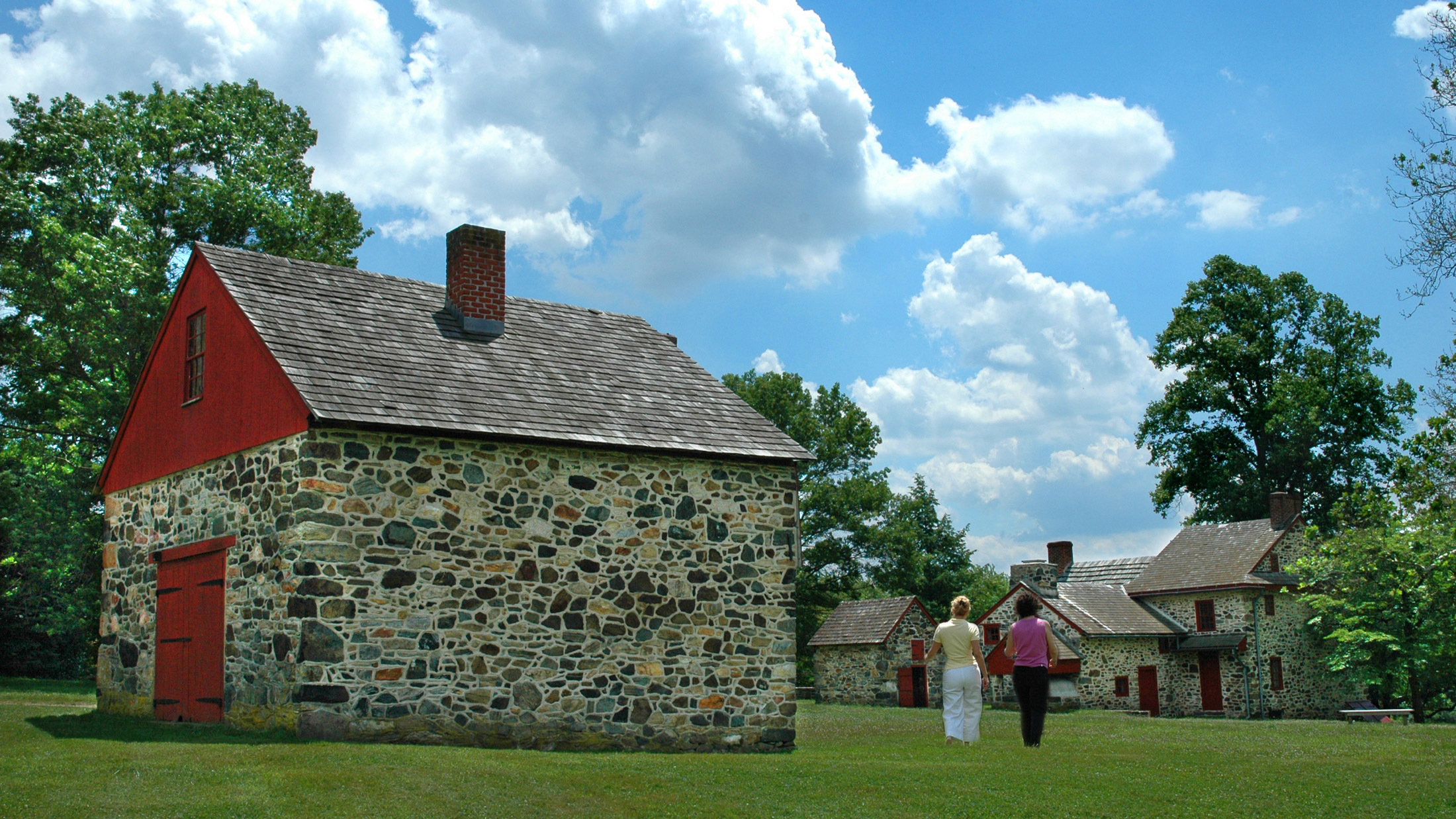 Two people walk past an old stone building with red painted door at Brandywine Battlefield Park.