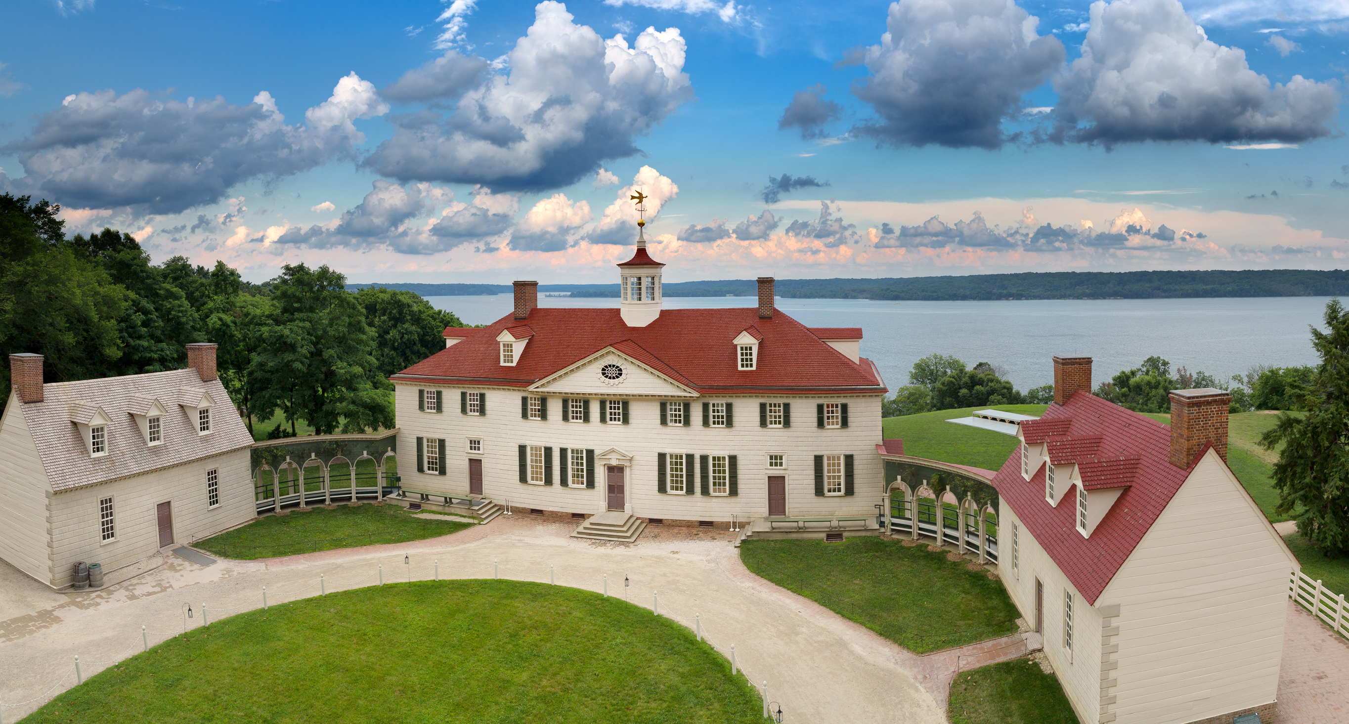 The Mount Vernon estate with green lawn in front and beige mansion with red roof and Potomac River in the background.