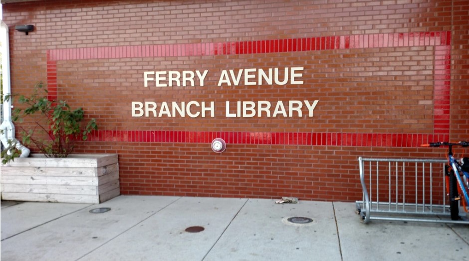 Bright red-orange brick facade with Ferry Avenue Branch Library text in white surrounded by a rectangle of bright red brick.